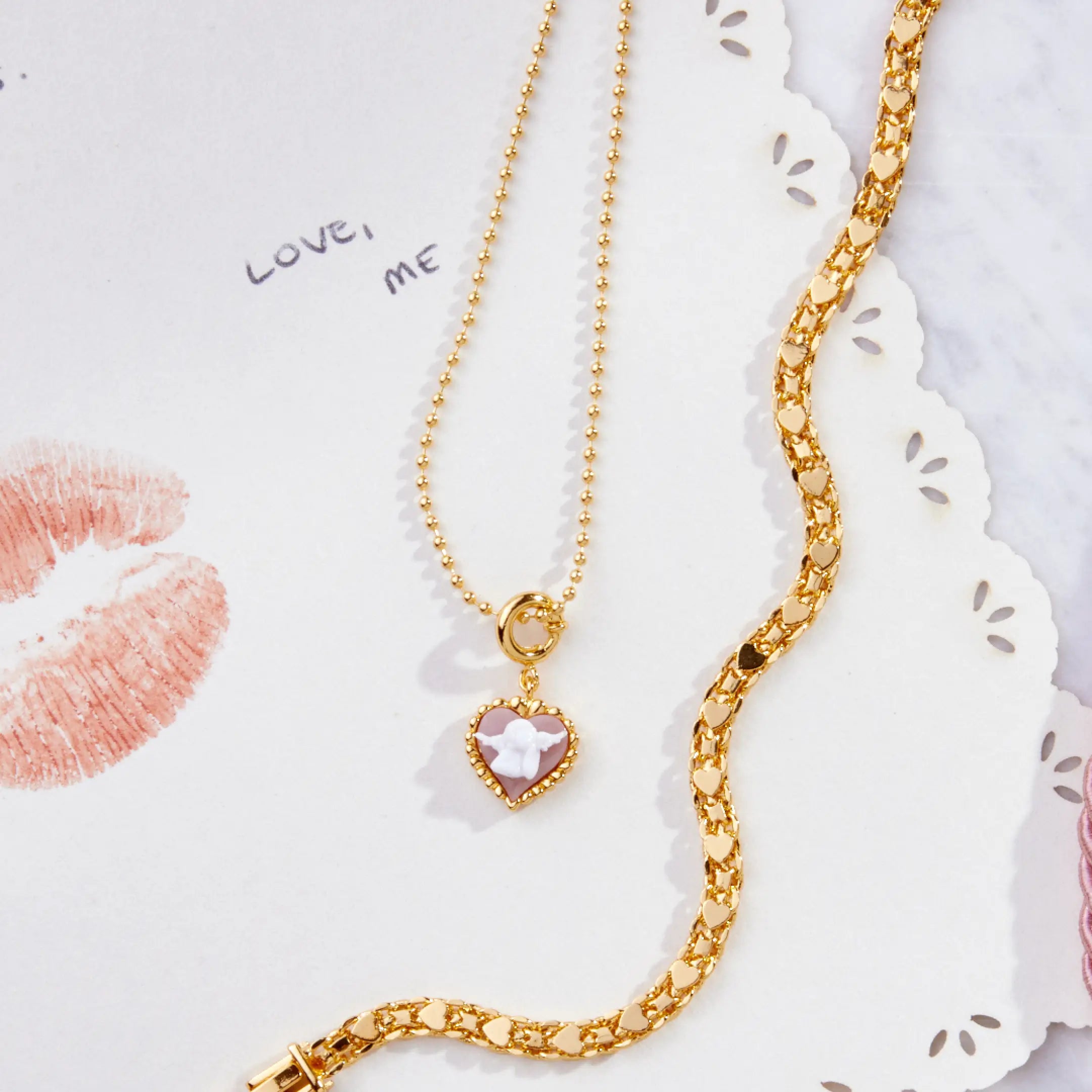 Gold necklace with a heart-shaped pendant on a decorative card with lips and 'LOVE, ME' text.