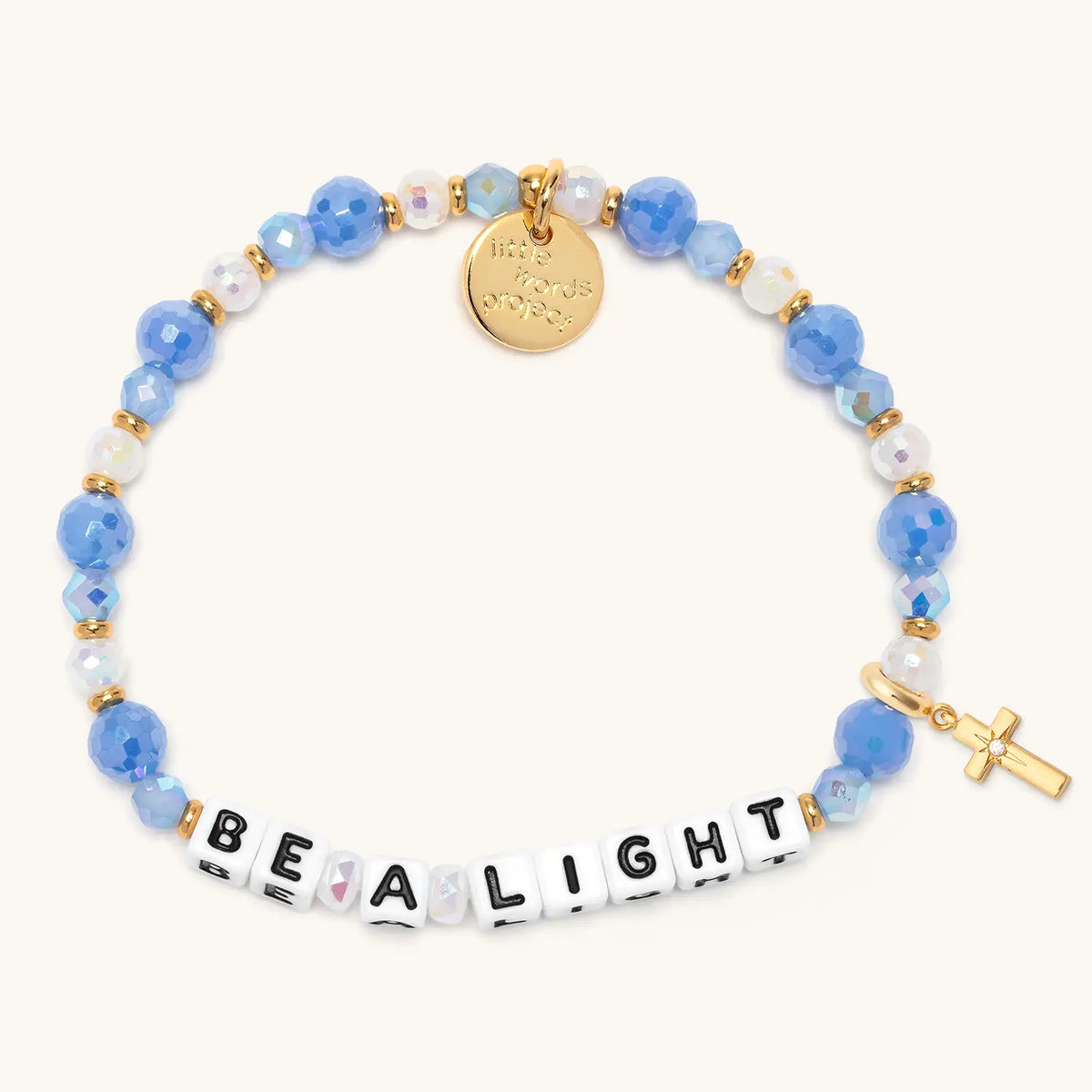 Be a Light bracelet in the Blizzard Baby bead pattern with white letter beads, gold puffy cross charm with a clear CZ stone, flat-lay on cream background