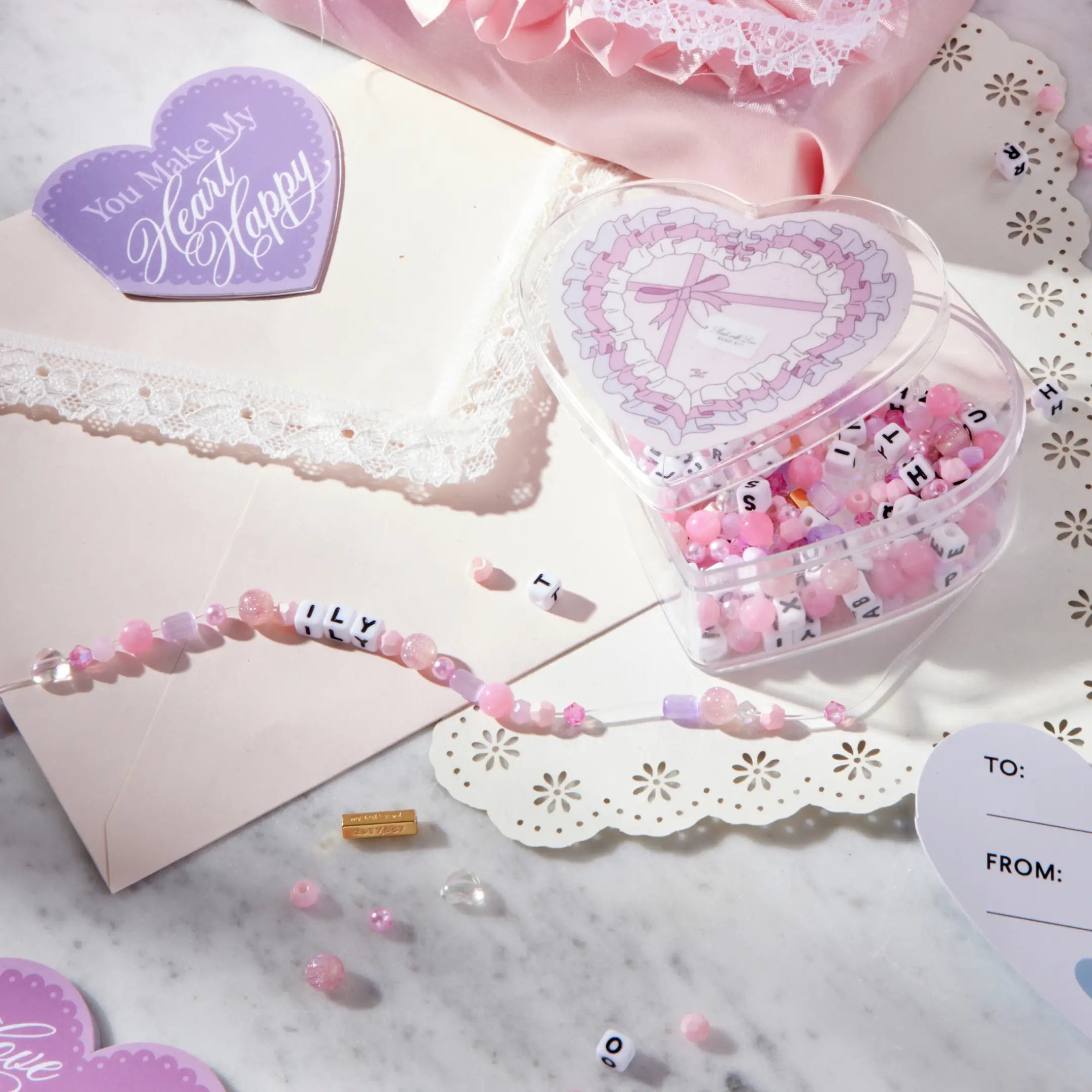 Heart-shaped container with decorative beads and a beaded bracelet on a marble surface.
