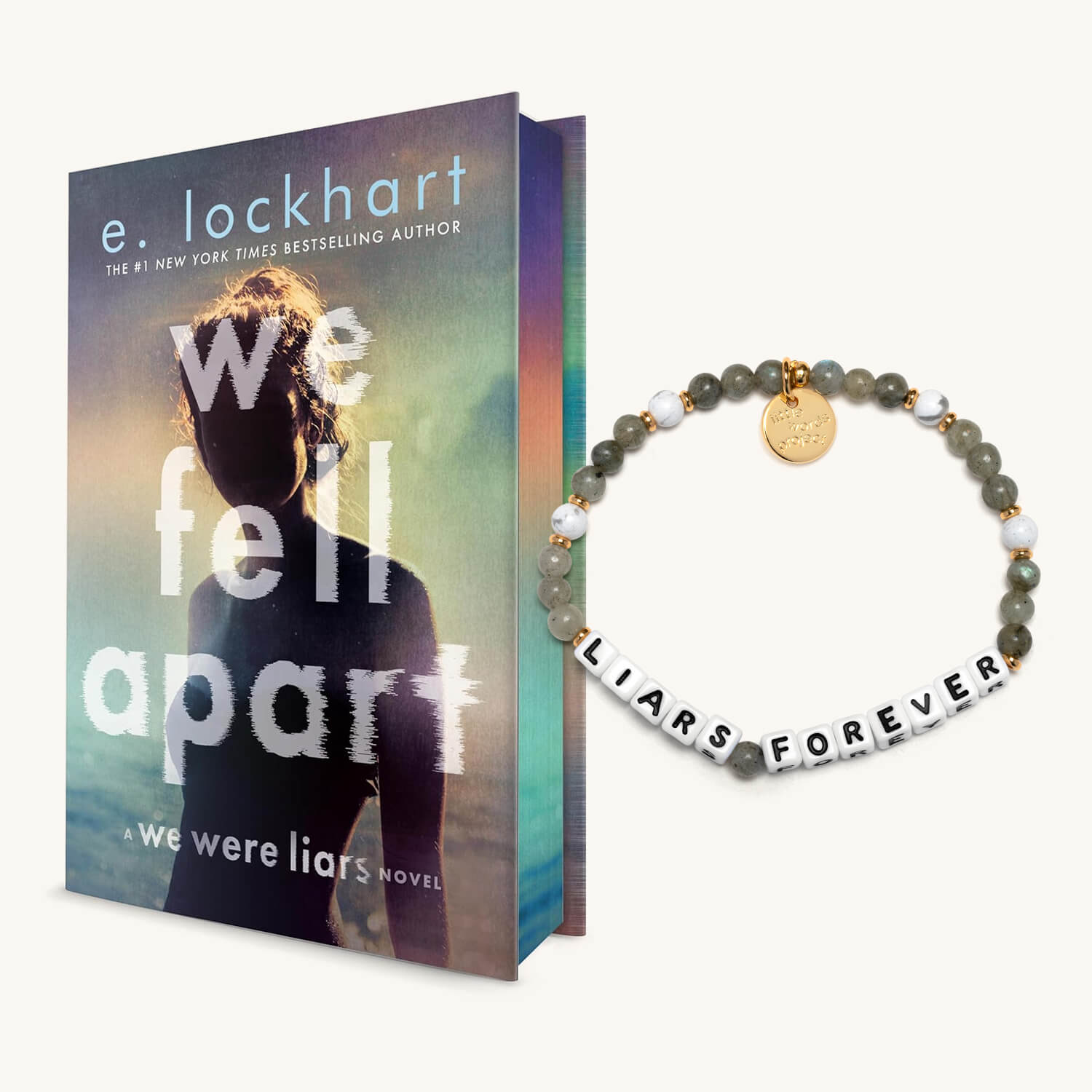 Book titled 'We Fall Apart' by e. lockhart with a bracelet labeled 'Liars Forever' on a white background