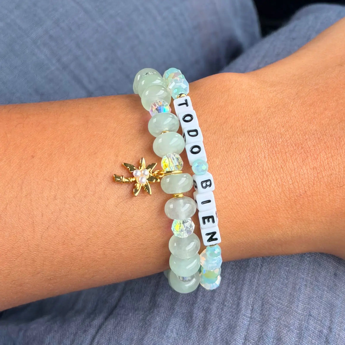 Close up of the Todo Bien Bracelet Set on wrist, mint green stone beads with clear crystals, white Todo Bien letter beads, and gold palm tree charm with pearl accent