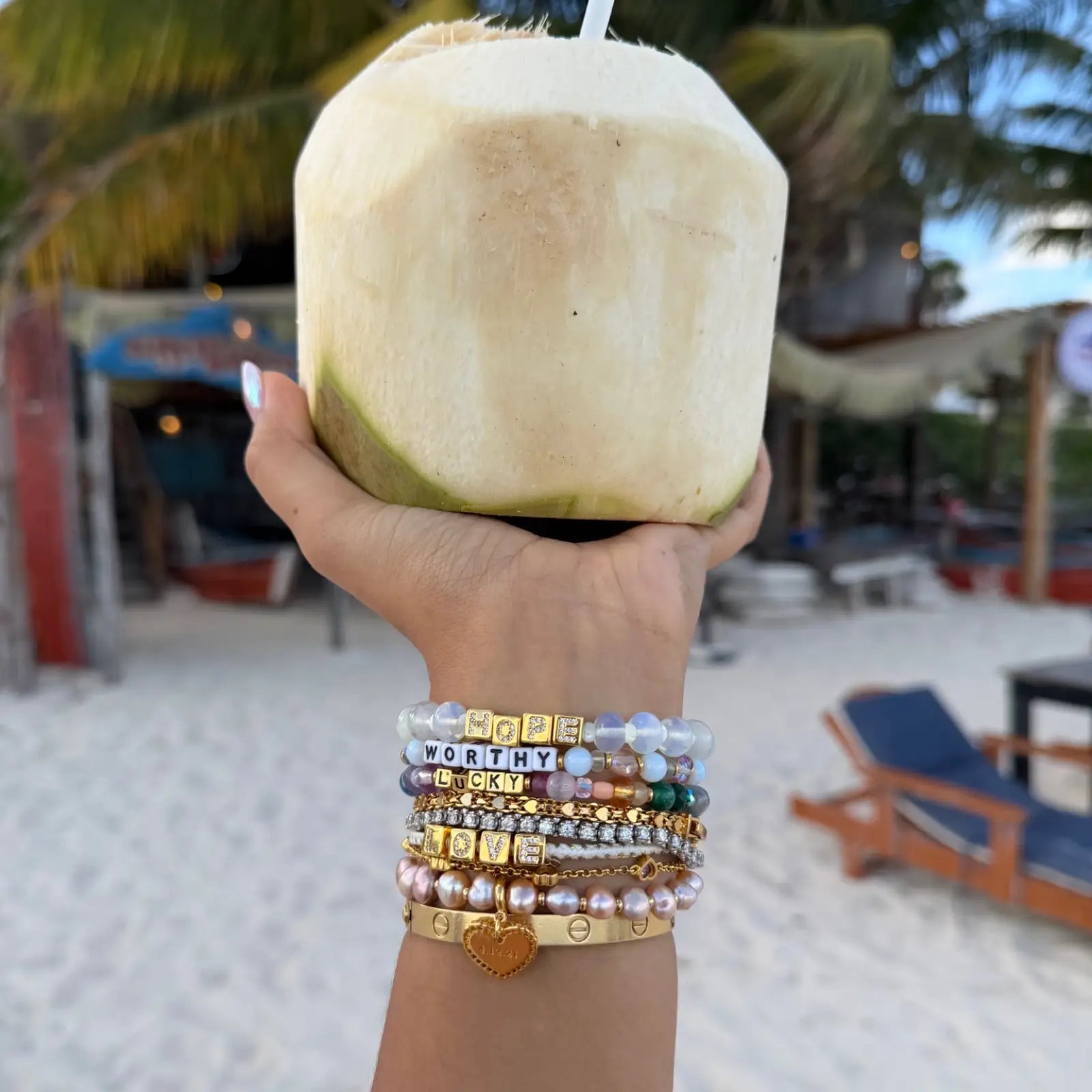 Hand holding a coconut with bracelets on a beach setting