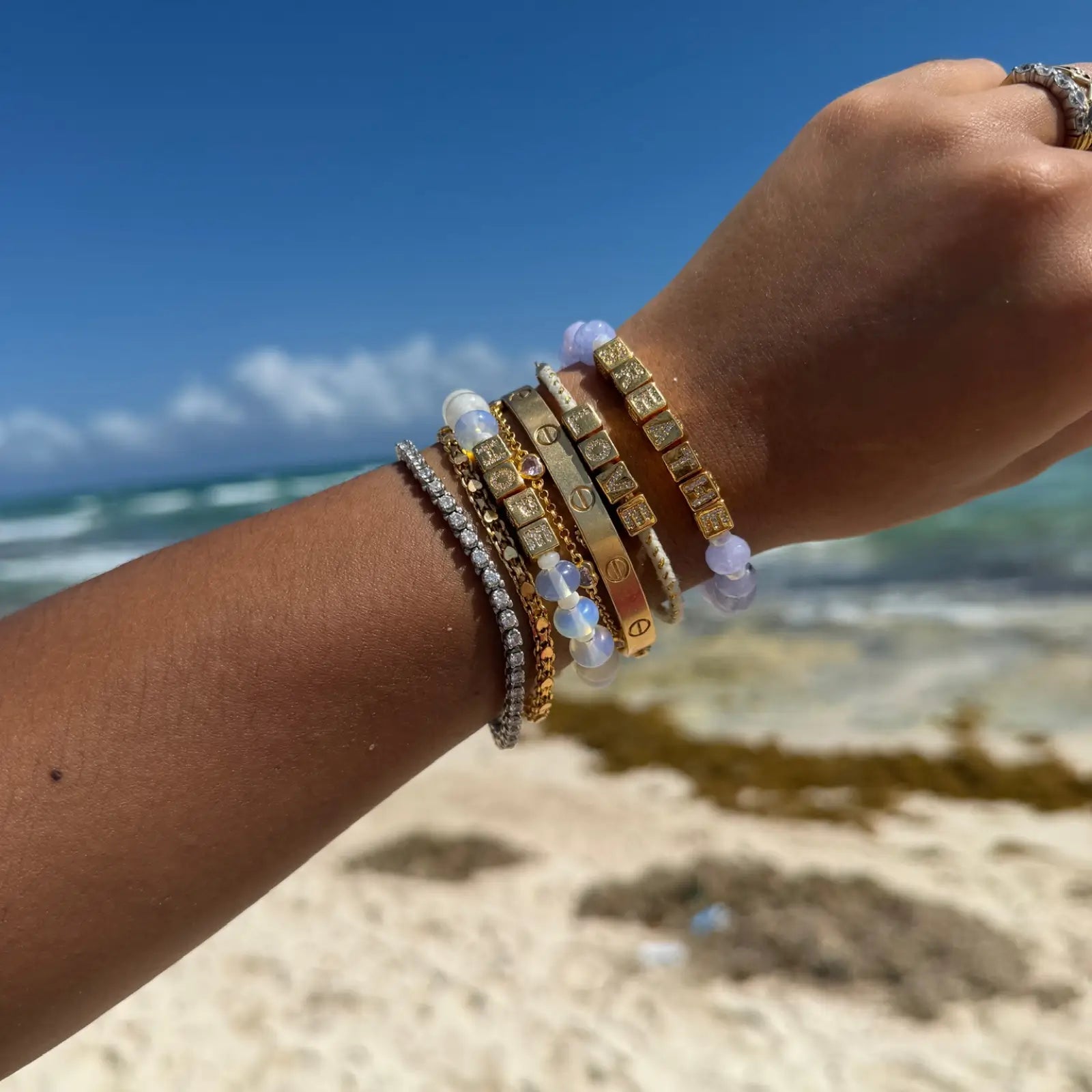 Hand wearing multiple bracelets with a beach background