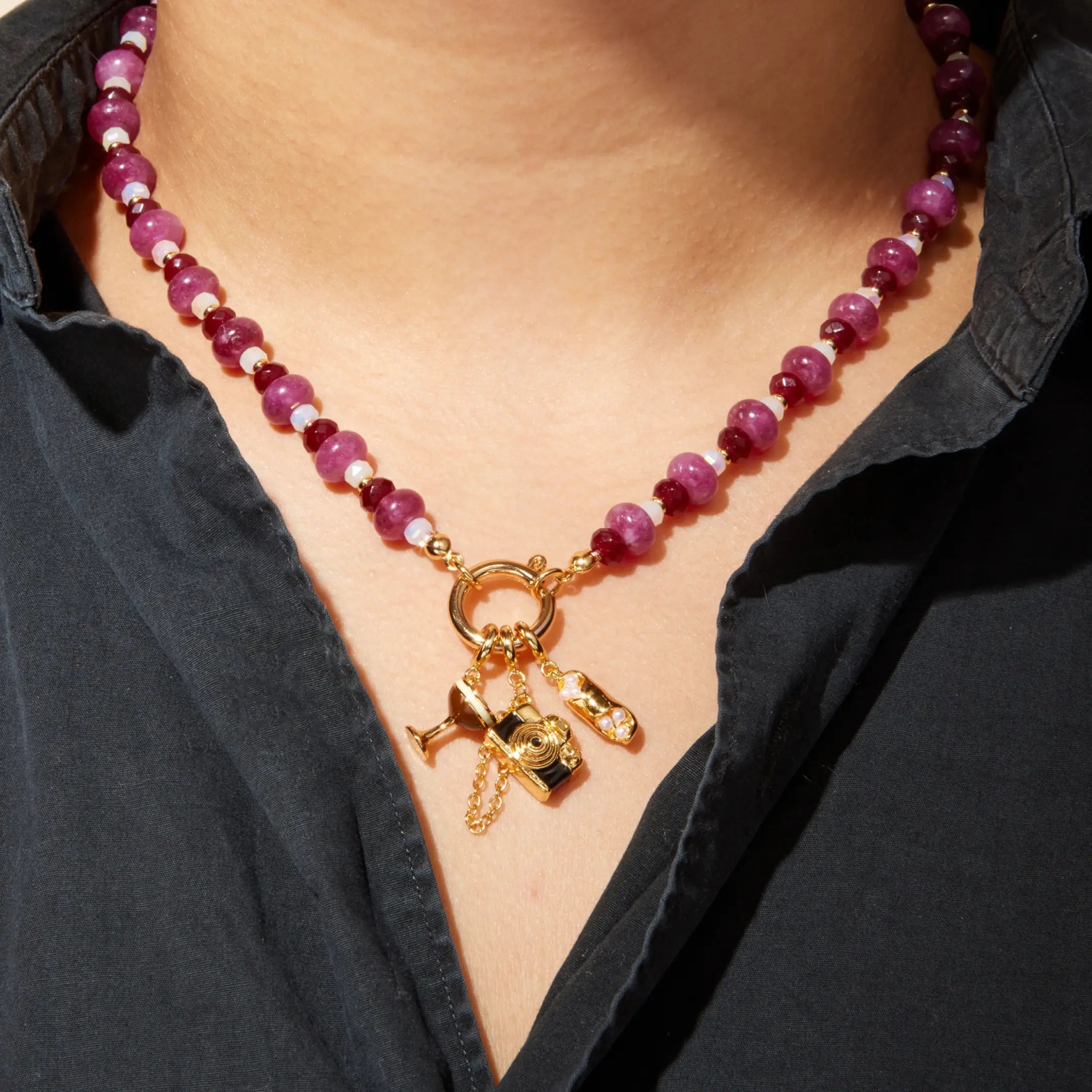 Necklace with pink beads and gold charms worn by a person against a black shirt background