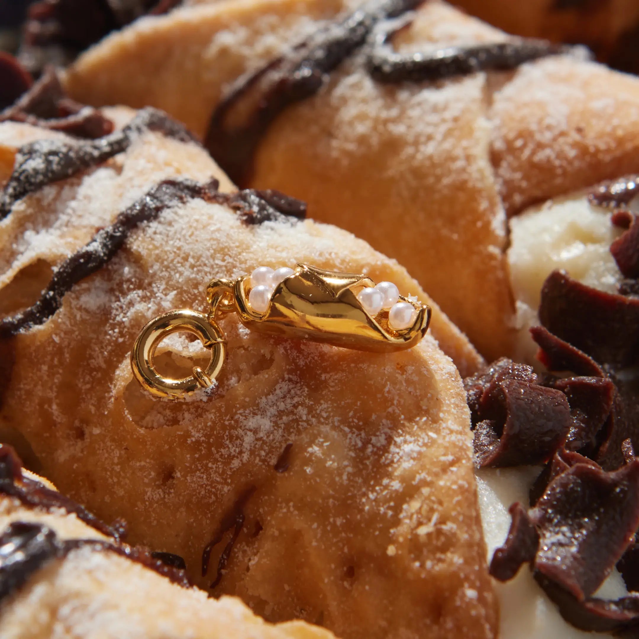 Gold cannoli charm with pearls on a dessert with chocolate and cream