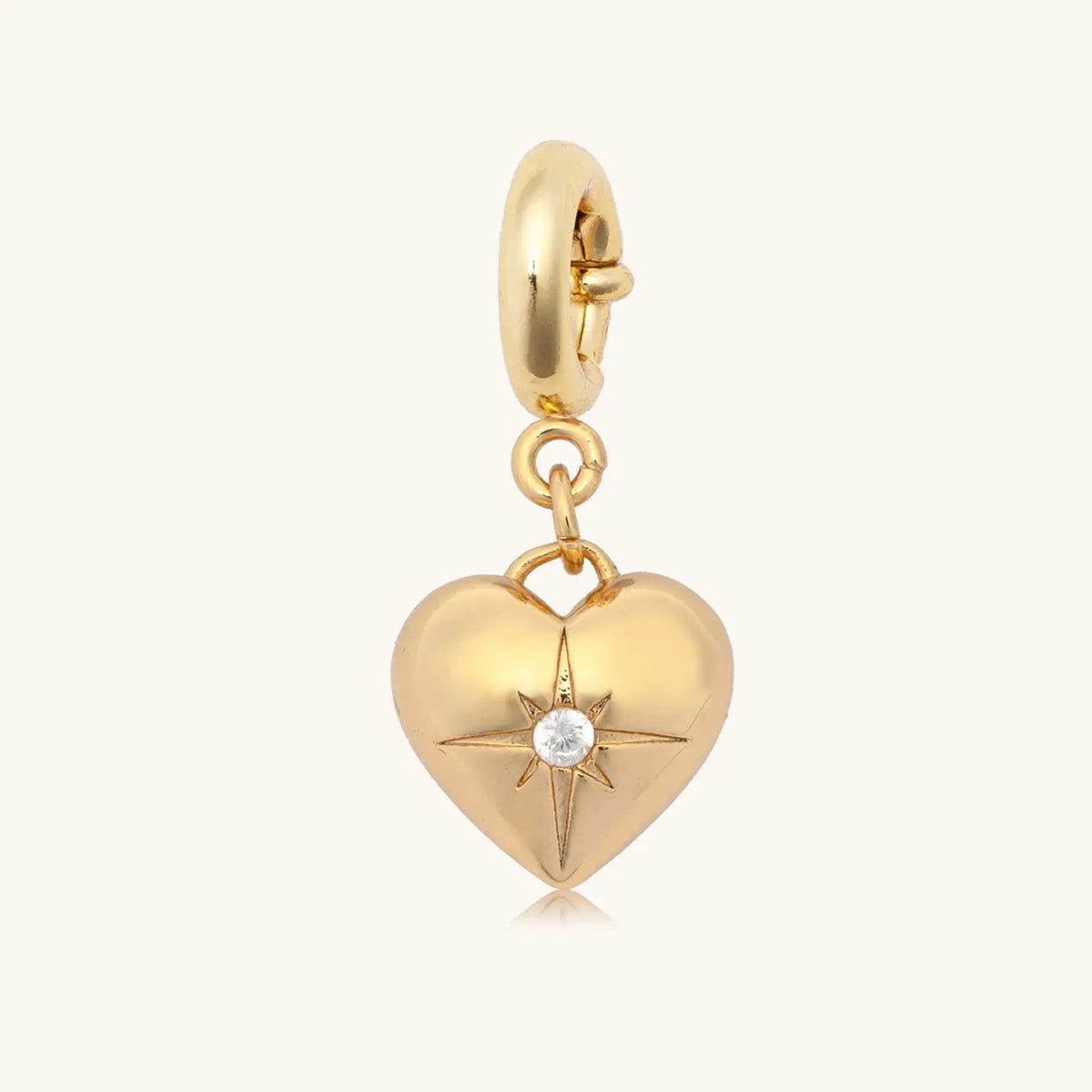 CZ Heart Charm, puffed gold heart charm with a single cz star set center, on a gold spring ring clasp, flat-lay on cream background