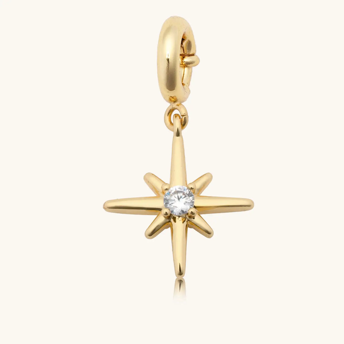 Starburst Charm from the Opal Light Charm Necklace set, gold starburst with a cz center, flat-lay on cream background