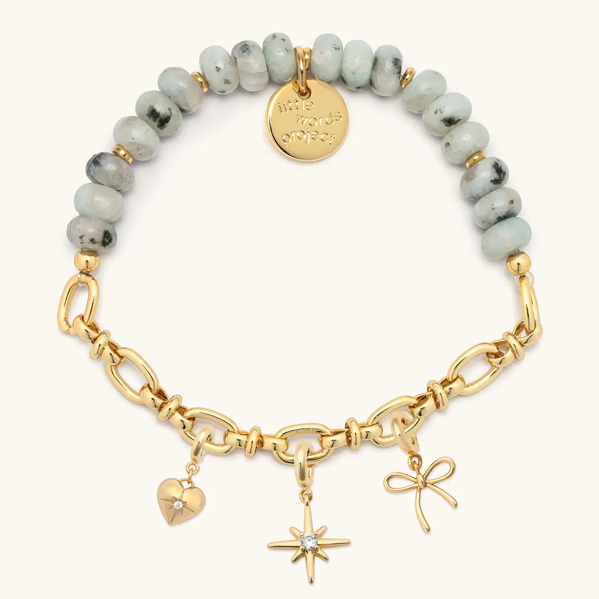 Smoky Ink Charm Bracelet Set with gold cz heart, starburst, and bow charms clipped onto the gold chain half of the bracelet, flat-lay on cream background