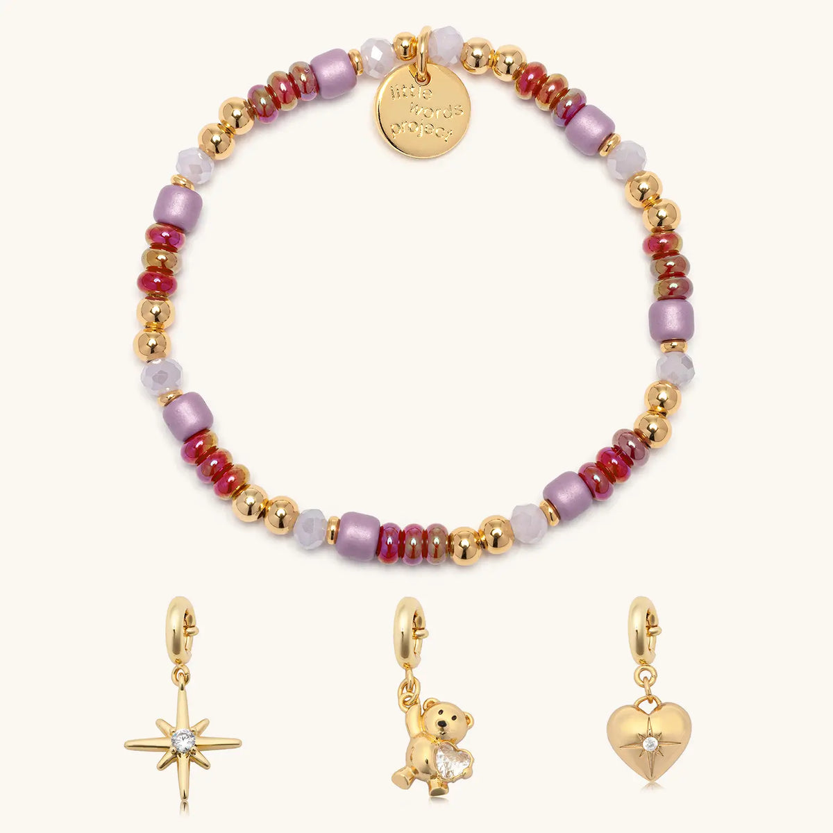 Golden Cherry Charm Bracelet set, Golden Cherry bracelet base in cherry red, lilac, and gold beads shown with gold starburst, teddy bear gem, and cz heart charms, flat-lay on cream background