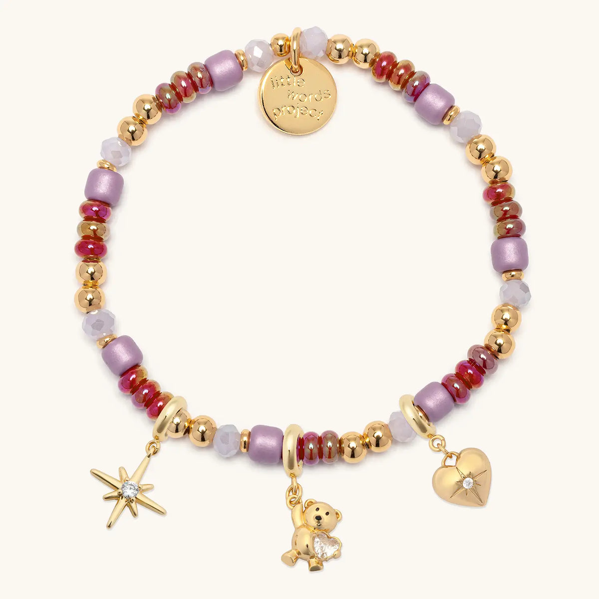 Golden Cherry Charm Bracelet with gold starburst, teddy bear gem, and cz heart charms clipped onto the cherry red, lilac, and gold beaded base, flat-lay on cream background