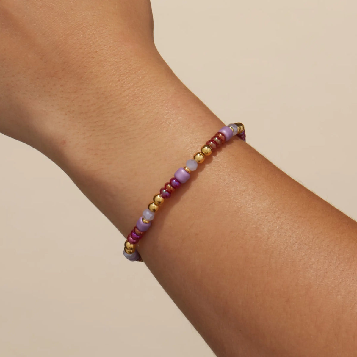 Golden Cherry Bracelet Base worn on a wrist, cherry red, lilac, and gold beads, on-model on a tan background