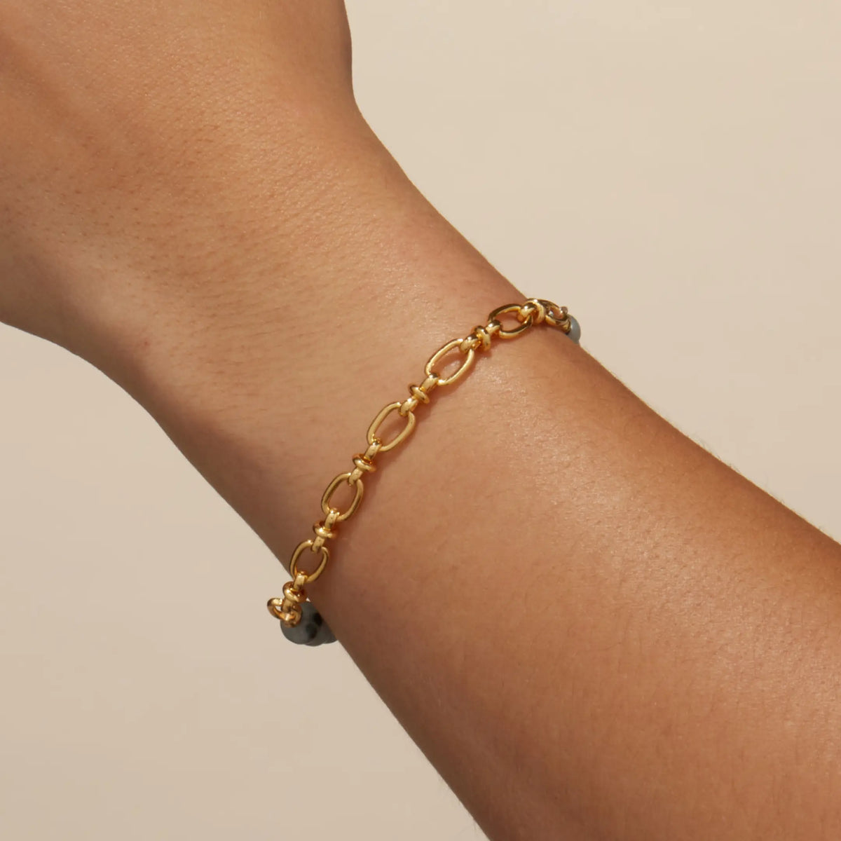 Smoky Ink Bracelet Base worn on a wrist, showing the gold link chain half of the half beaded, half chain bracelet, on-model on a tan background