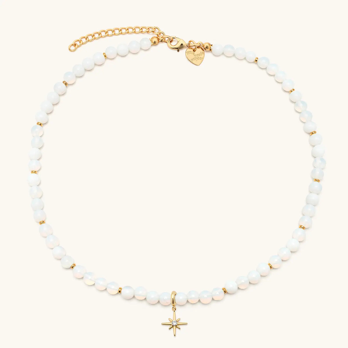 Opal Light Charm Necklace with the gold starburst charm clipped on, white beads with gold accents and gold extender chain, flat-lay on cream background