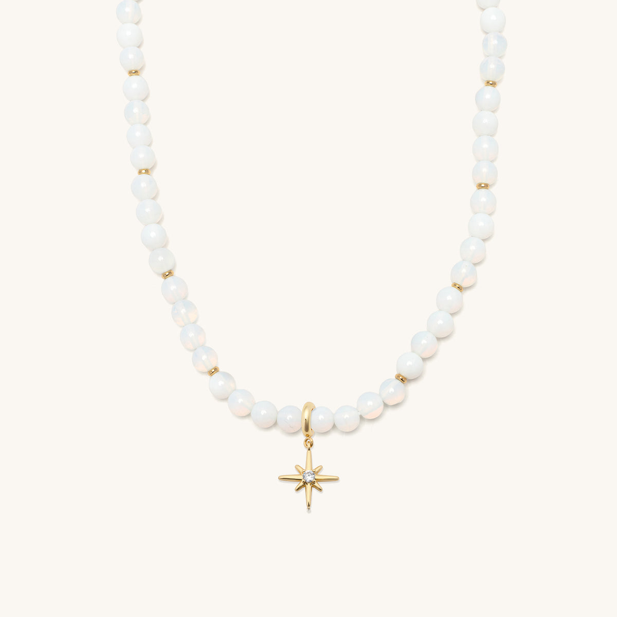 Opal Light Charm Necklace Set, glowing white beaded Opal Light necklace with gold spacers and the gold starburst charm clipped at the center, flat-lay on cream background