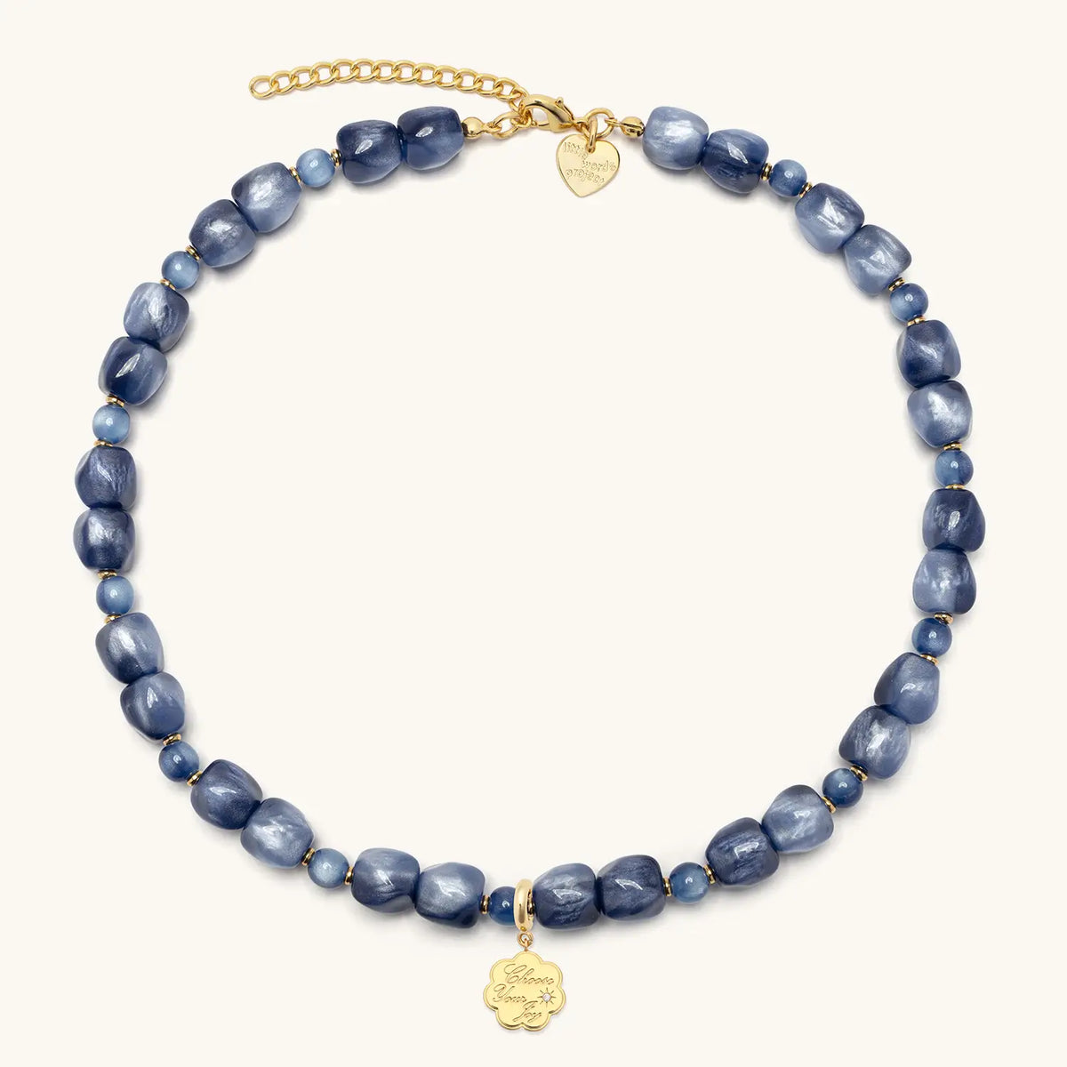 Radio Fever Charm Necklace with the gold Choose Your Joy coin charm clipped on, shimmery blue beads and gold extender chain, flat-lay on cream background