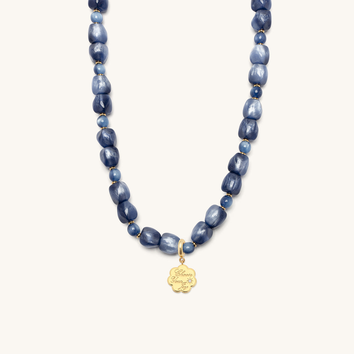 Radio Fever Charm Necklace Set, shimmery blue beaded Radio Fever necklace with the gold Choose Your Joy coin charm clipped at the center, flat-lay on cream background