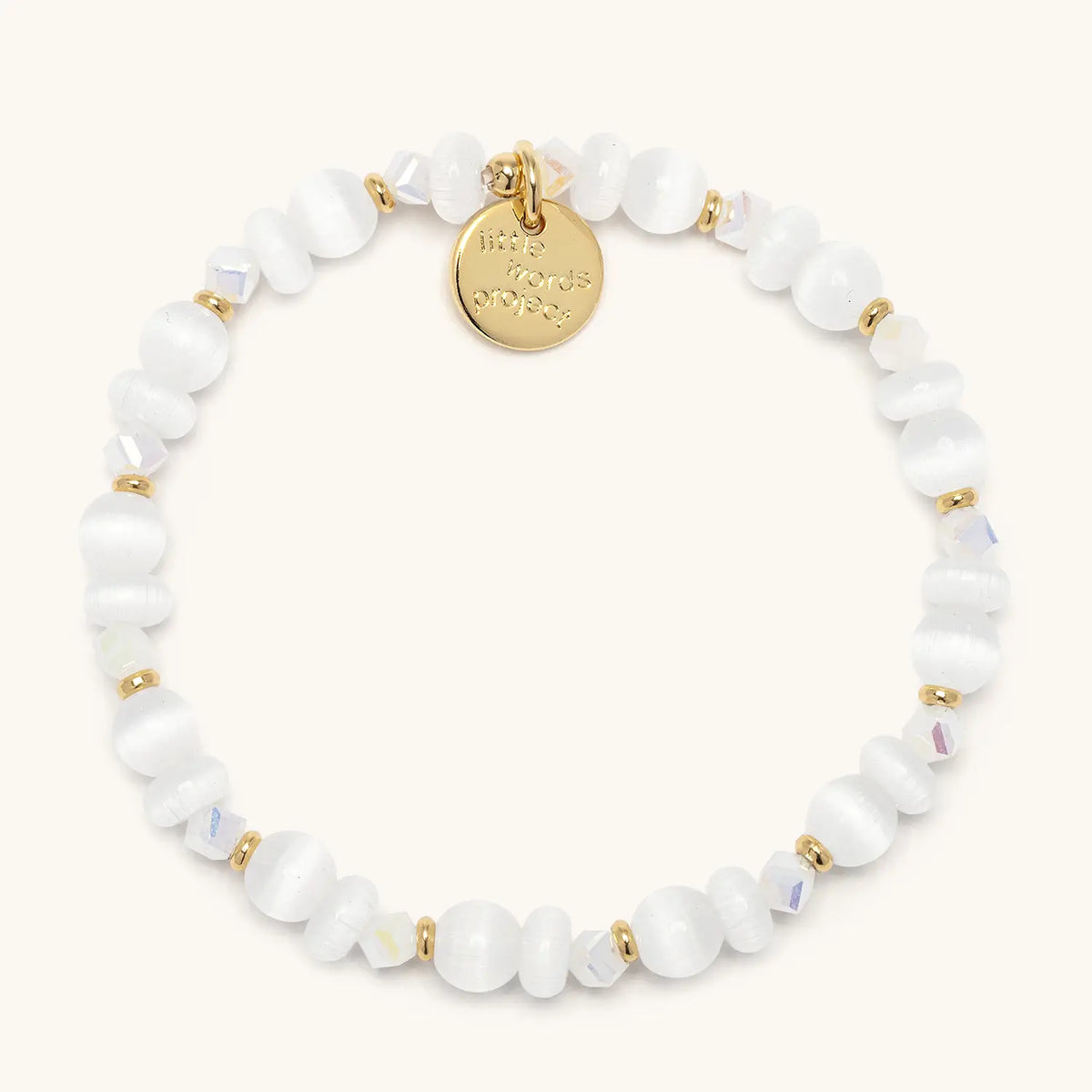 Arctic Honey Bracelet Base in the Arctic Honey bead pattern, milky white cat eye beads with clear iridescent crystals, gold accents, and a gold logo coin tag, flat-lay on cream background