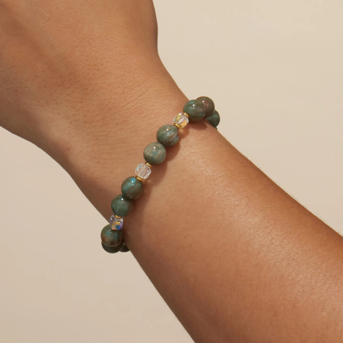 Velvet Voltage Bracelet Base worn on a wrist, marbled sage green beads with clear crystal accents, on-model on a tan background