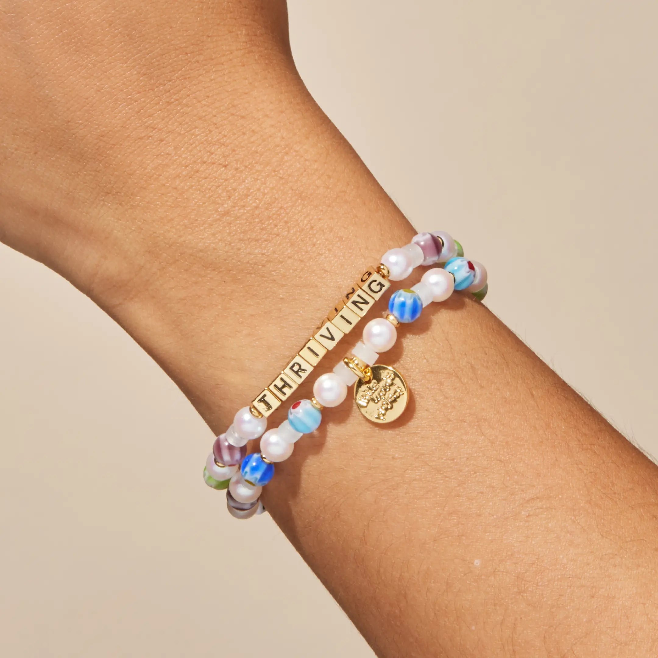 Multicolored beaded bracelet with gold tag on a wrist against a beige background