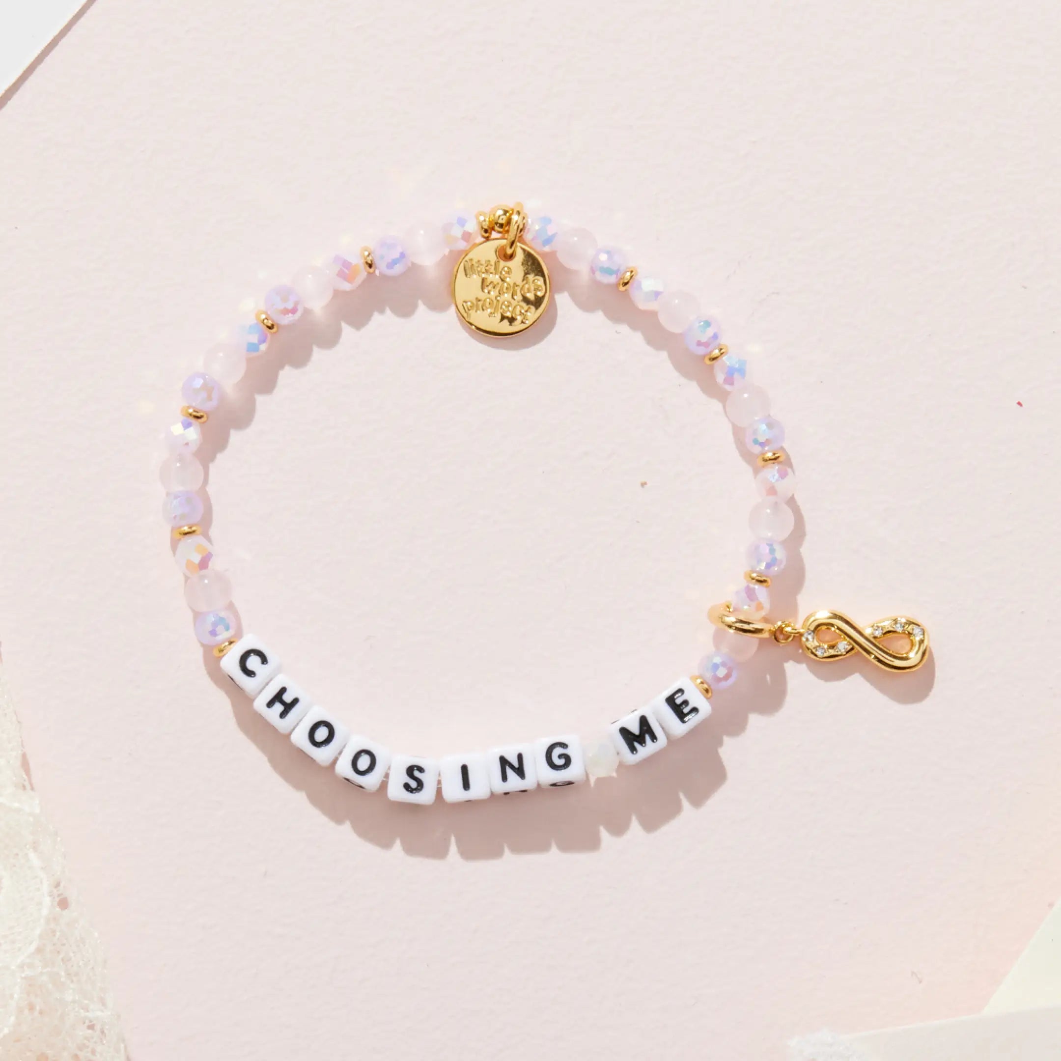 Bracelet with letter beads spelling 'CHOOSING ME' on a light pink background