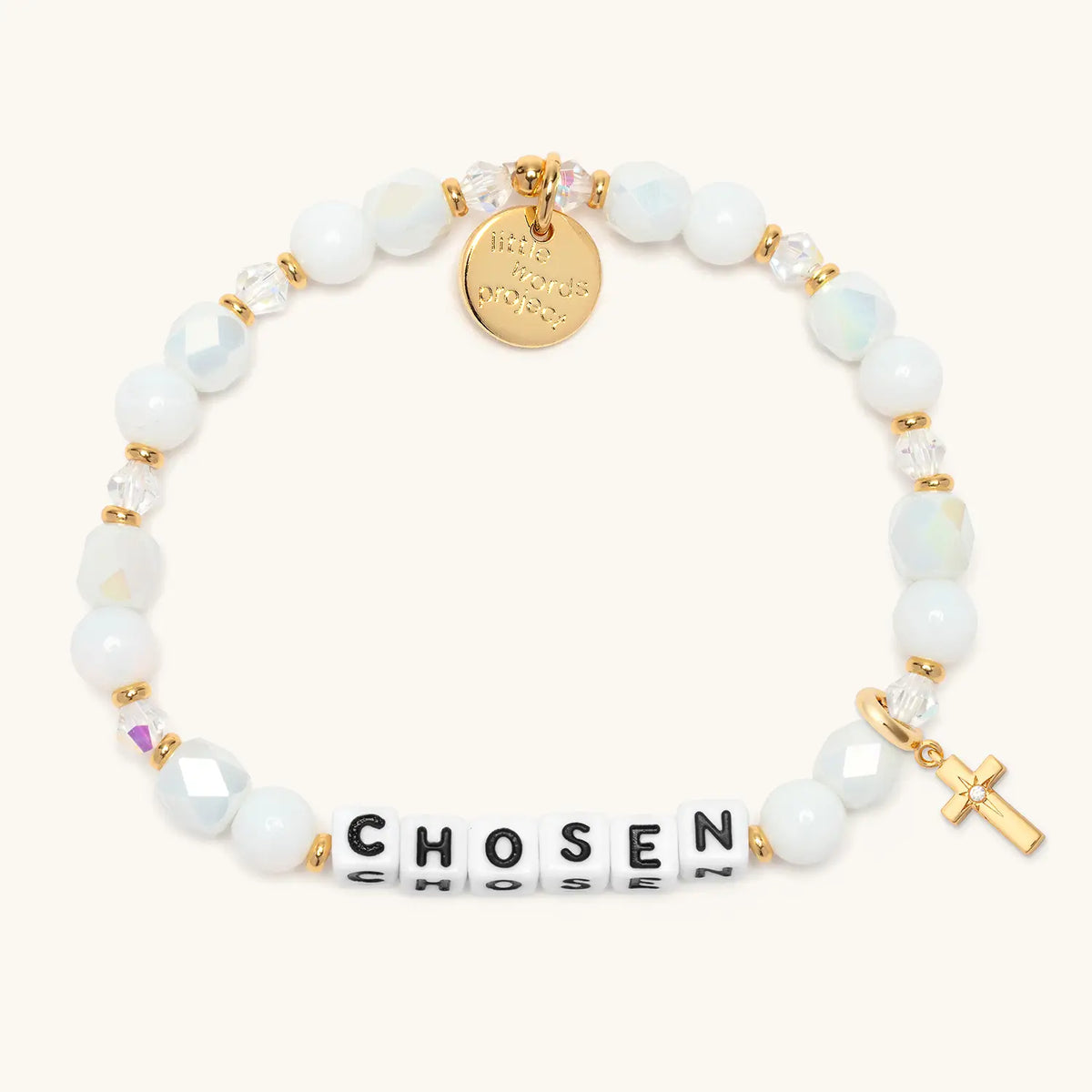Chosen bracelet in the Snow Fantasy bead pattern with white letter beads, gold puffy cross charm with a clear CZ stone, flat-lay on cream background