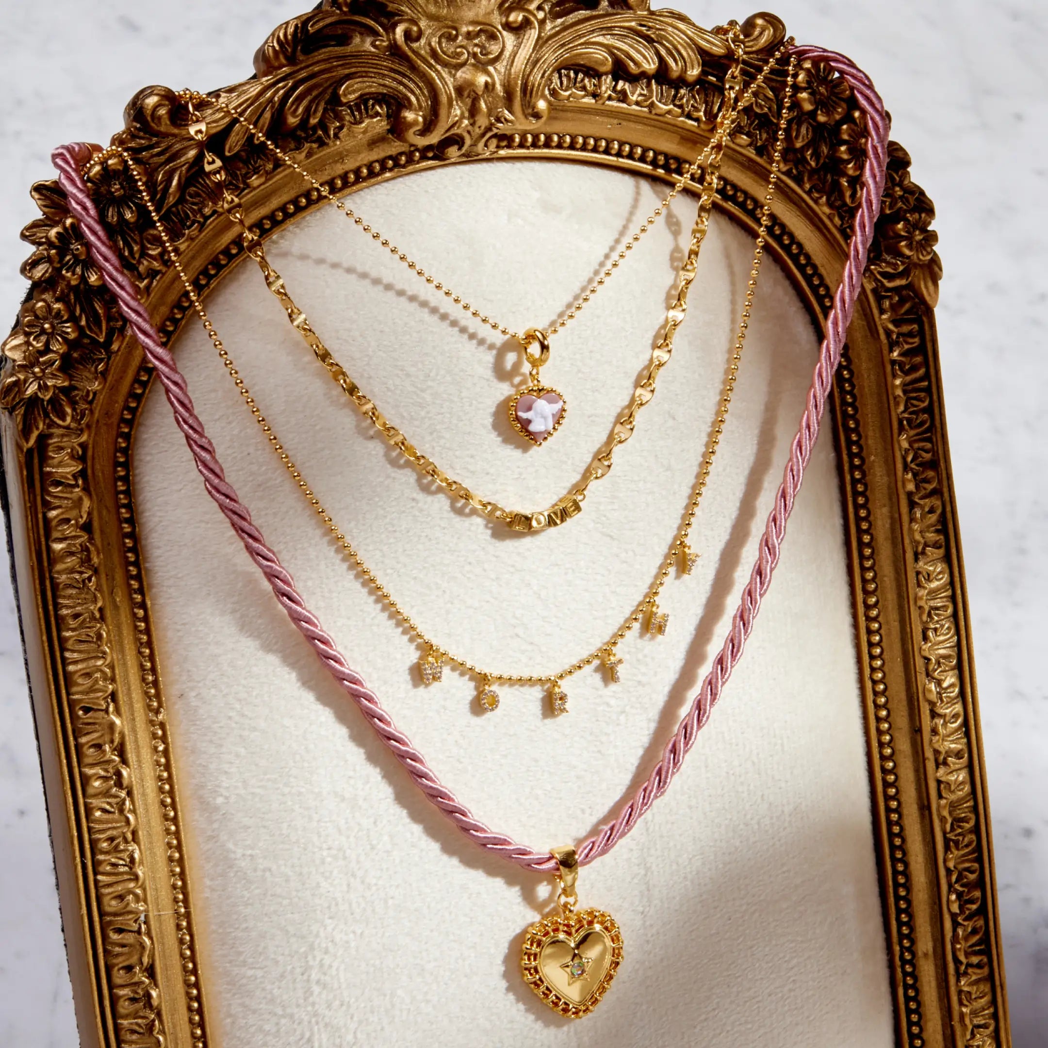 Gold necklaces with pink cord on a decorative stand