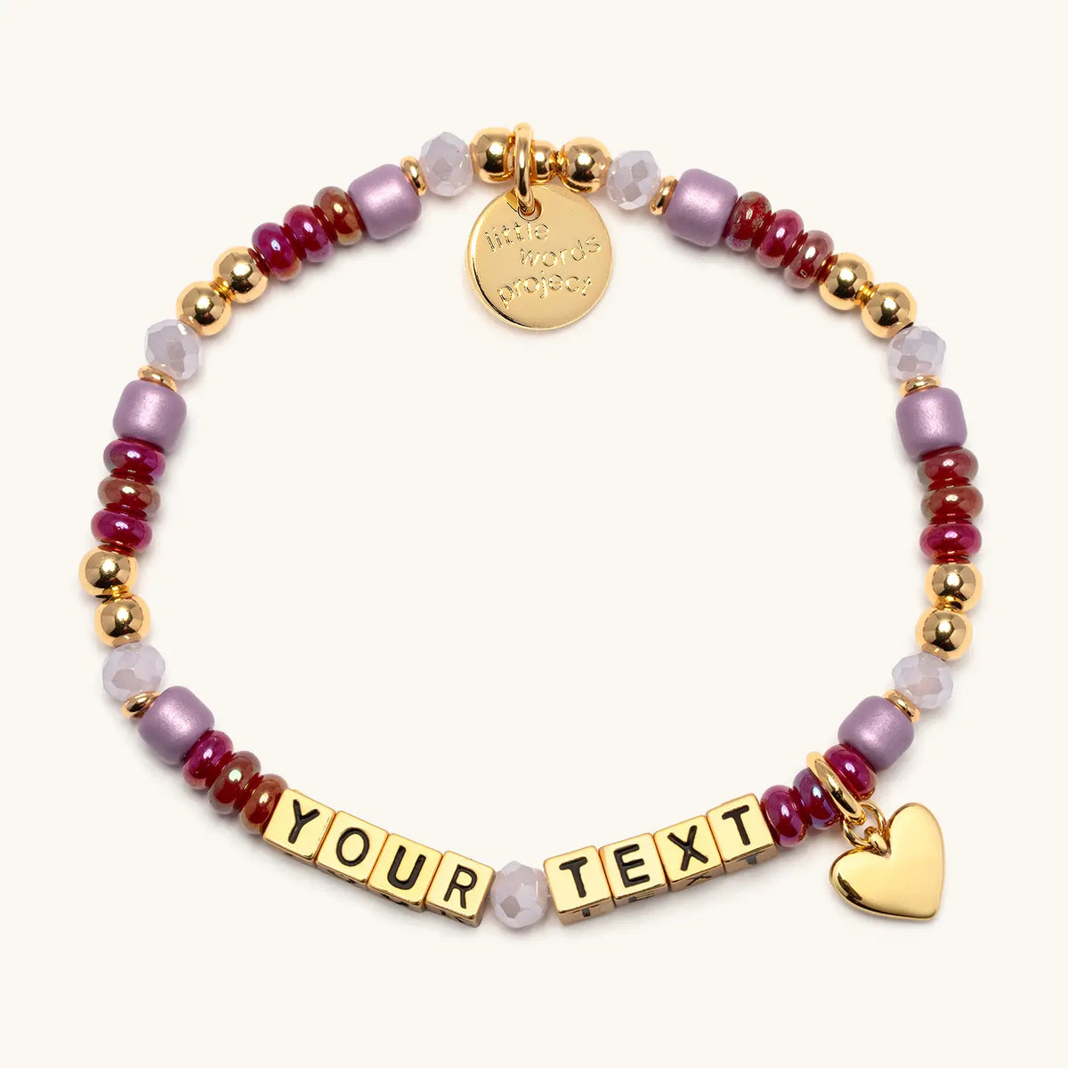 Custom Golden Cherry bracelet in the Golden Cherry bead pattern, gold letter beads reading Your Text, cranberry red, mauve, and blush beads with gold beads and a gold heart charm, flat-lay on cream background