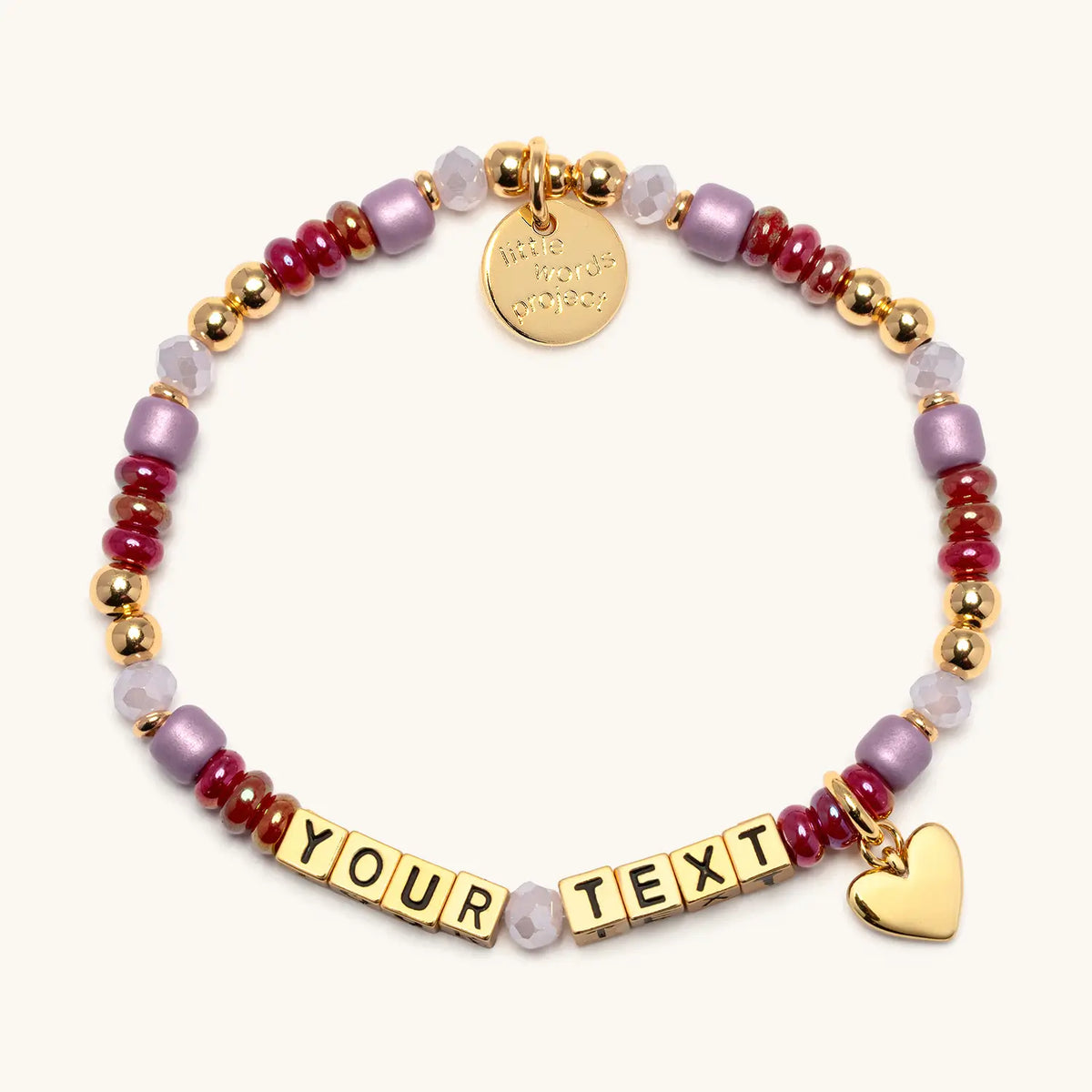 Custom Golden Cherry bracelet in the Golden Cherry bead pattern, gold letter beads reading Your Text, cranberry red, mauve, and blush beads with gold beads and a gold heart charm, flat-lay on cream background
