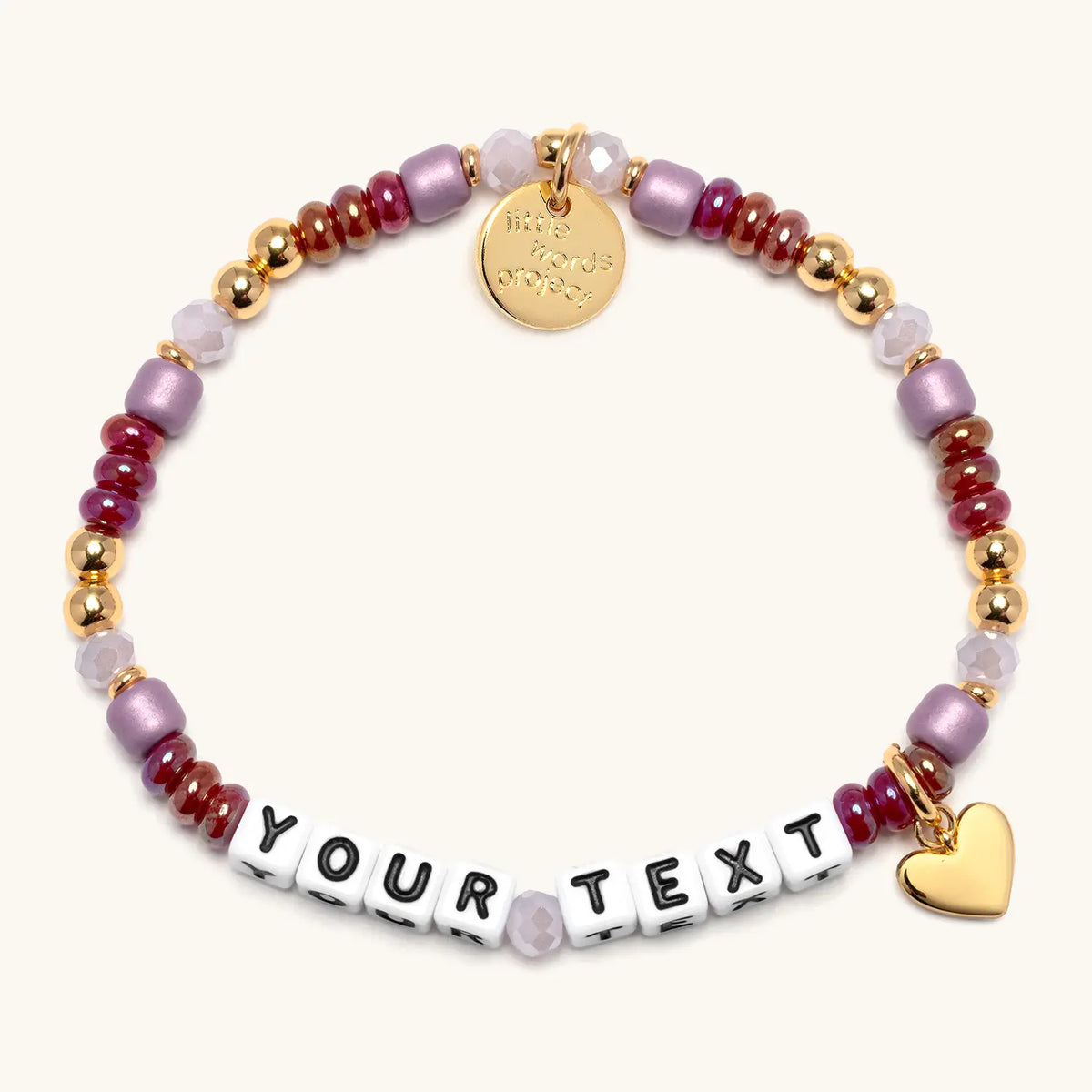 Custom Golden Cherry bracelet in the Golden Cherry bead pattern, white letter beads reading Your Text, cranberry red, mauve, and blush beads with gold beads and a gold heart charm, flat-lay on cream background