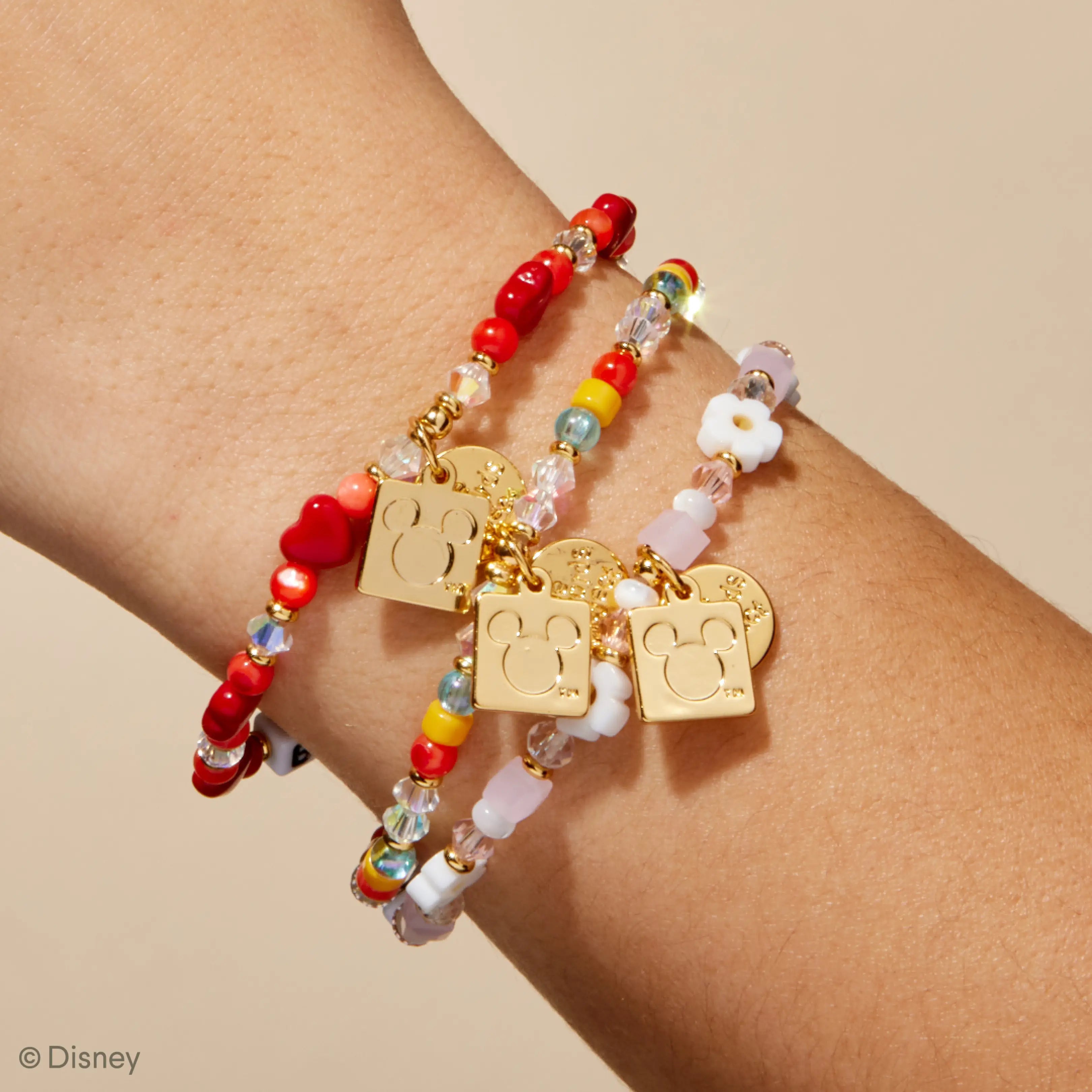 Bracelet with colorful beads and gold tags on a wrist against a beige background