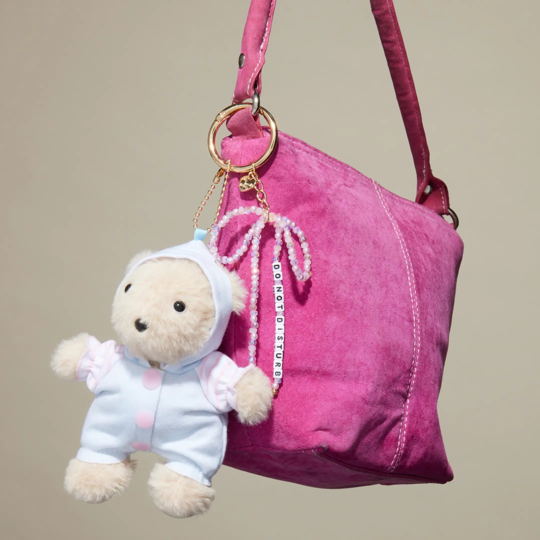 Do Not Disturb plush bear bag charm clipped to a pink suede tote