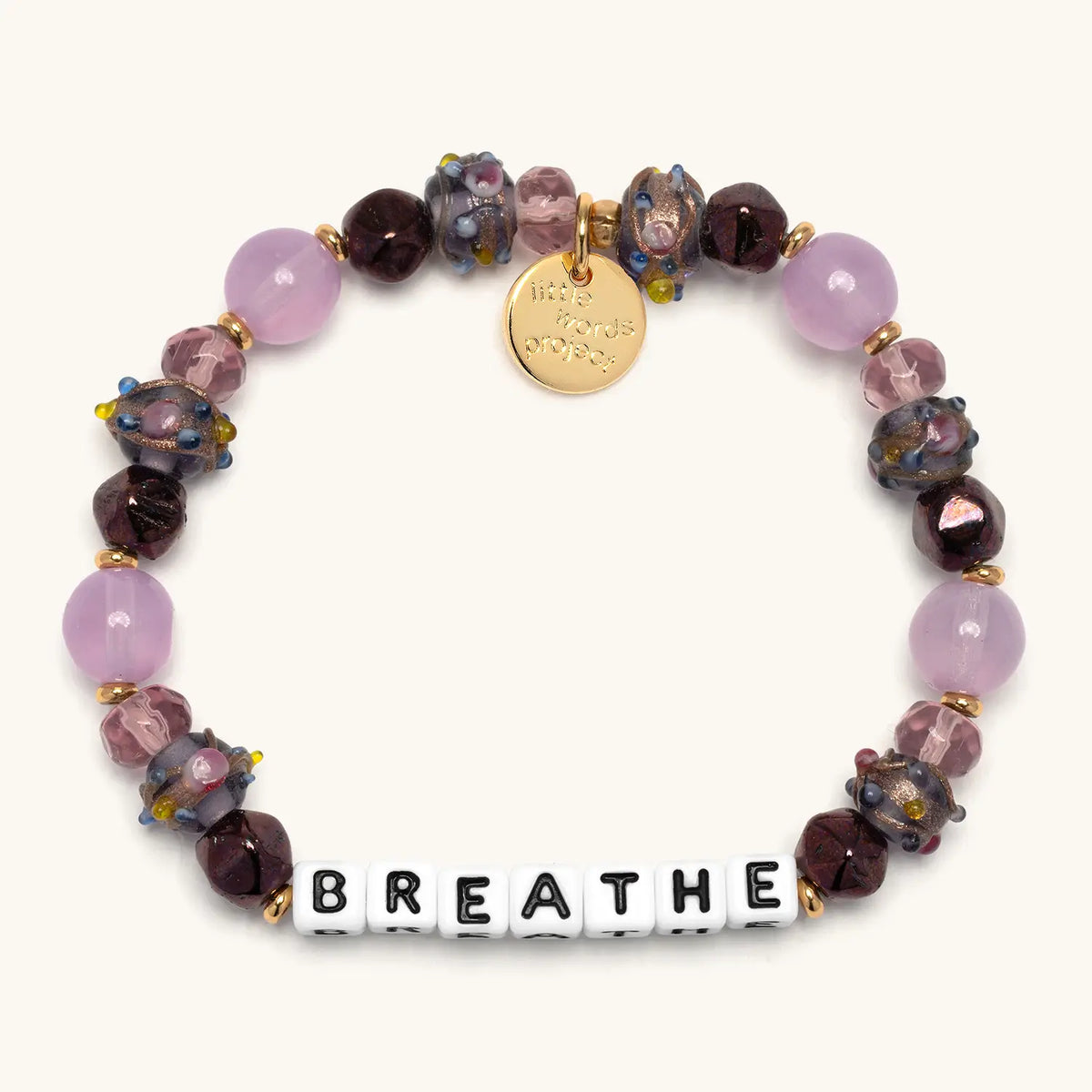 Breathe bracelet in the Autumn Glow bead pattern, white letter beads with lavender jade beads, deep plum faceted crystals, and floral glass beads with gold accents, flat-lay on cream background
