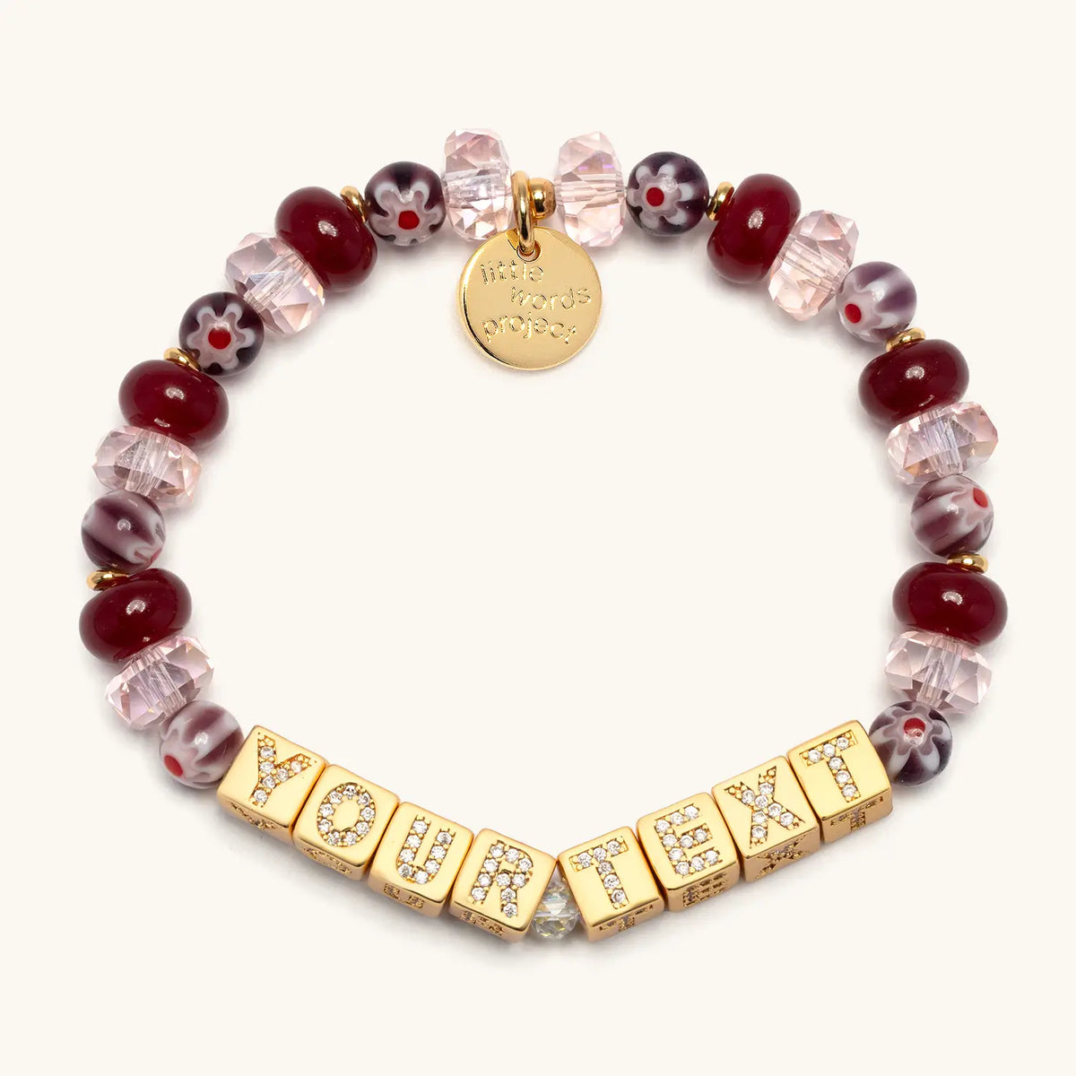 BOLDER Custom Rosemary bracelet with gold CZ letter blocks reading Your Text, raspberry jade beads, blush faceted crystals, and plum floral glass beads with gold accents, flat-lay on cream background