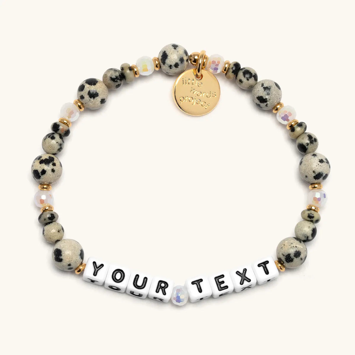 Custom Dot Vibes bracelet with white letter beads reading Your Text, dalmatian jasper stone beads and iridescent crystals with gold accents, flat-lay on cream background