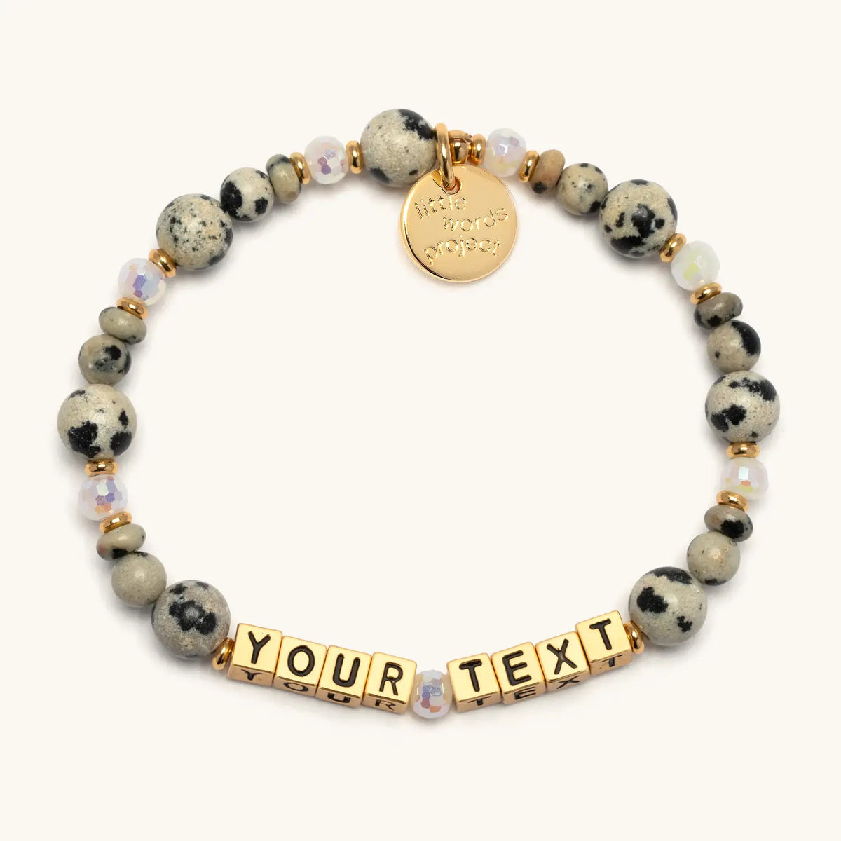 Custom Dot Vibes bracelet with gold letter beads reading Your Text, dalmatian jasper stone beads and iridescent crystals with gold accents, flat-lay on cream background