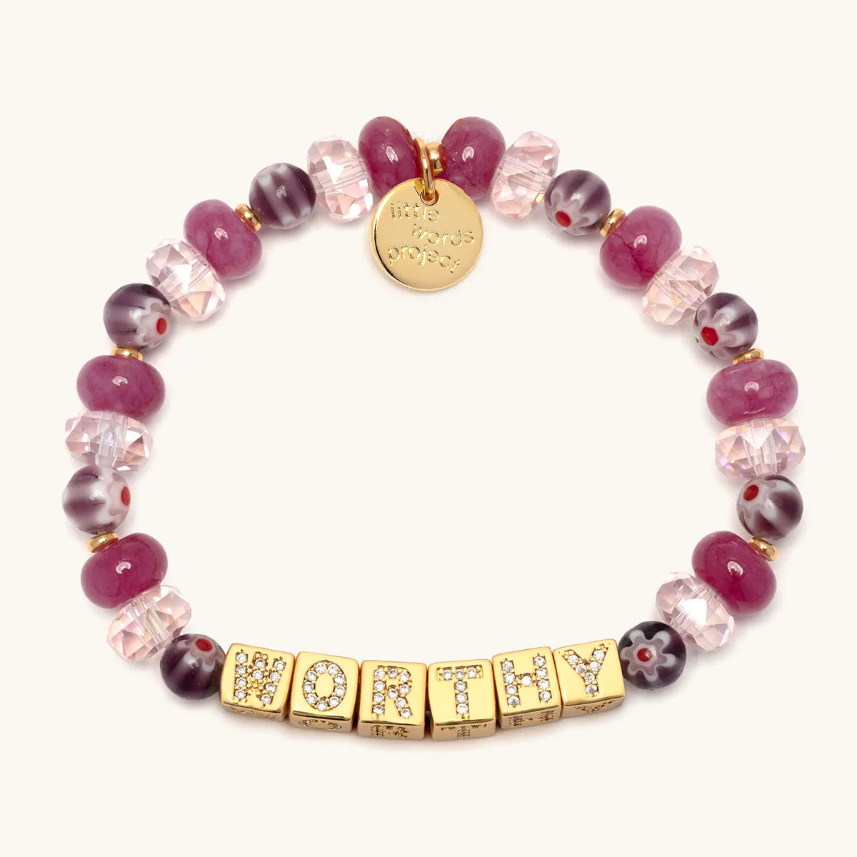 BOLDER Worthy Bracelet in the Rosemary bead pattern, gold CZ letter blocks with raspberry jade beads, blush faceted crystals, and plum floral glass beads with gold accents, flat-lay on cream background