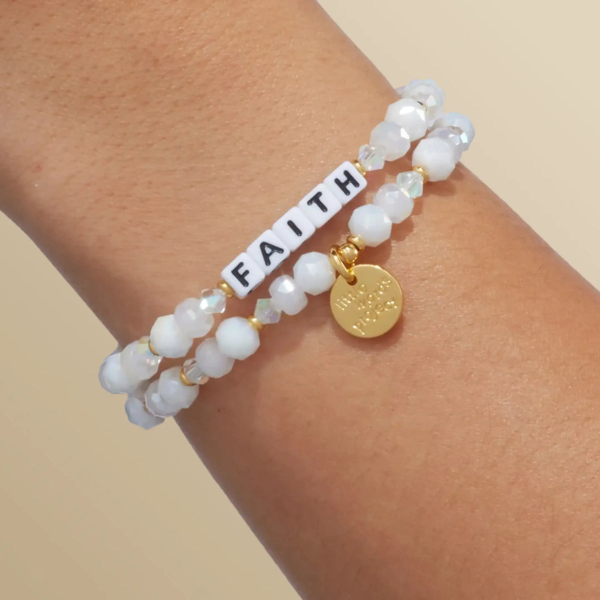 Faith bracelet in the Snowflake Sparkle bead pattern with white letter beads, stacked with a second bracelet, on-model wrist shot on warm neutral background