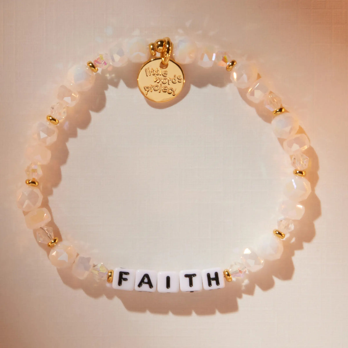 Faith bracelet in the Snowflake Sparkle bead pattern with white letter beads, flat-lay on warm neutral background with soft light