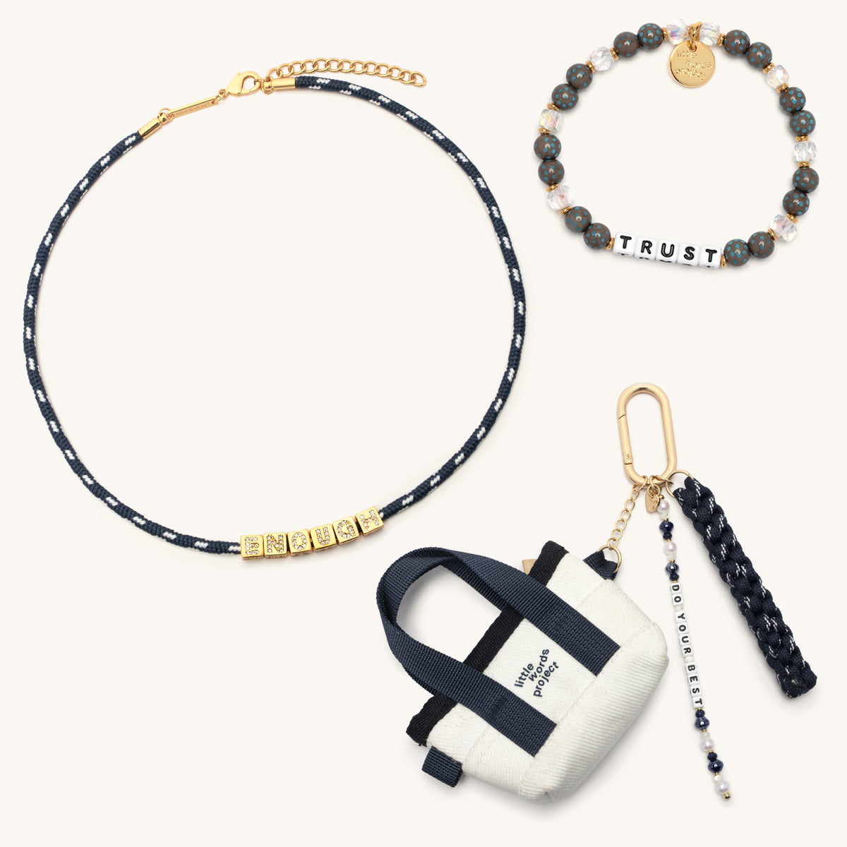 Fall Founder Faves Set flat-lay on cream background showing the Trust bracelet in white letter beads with gray speckled and clear crystal beads, the BOLDER Enough paracord necklace in navy with gold CZ letter blocks, and the Do Your Best Bag Charm with mini canvas tote, navy paracord tassel, and pearl beaded word strand