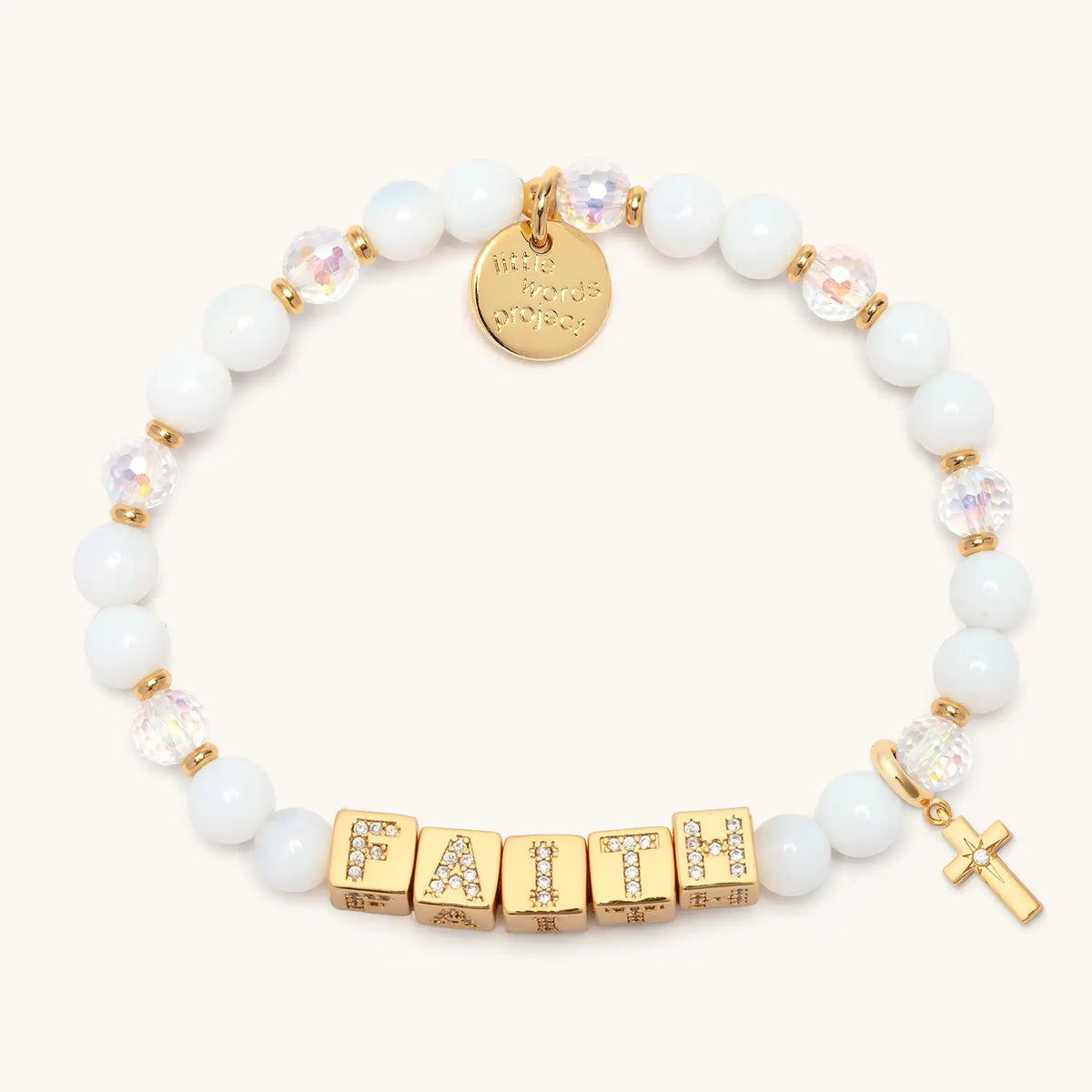 BOLDER Faith Bracelet in the Icicle Energy bead pattern with gold CZ letter blocks, gold puffy cross charm with a clear CZ stone, flat-lay on cream background