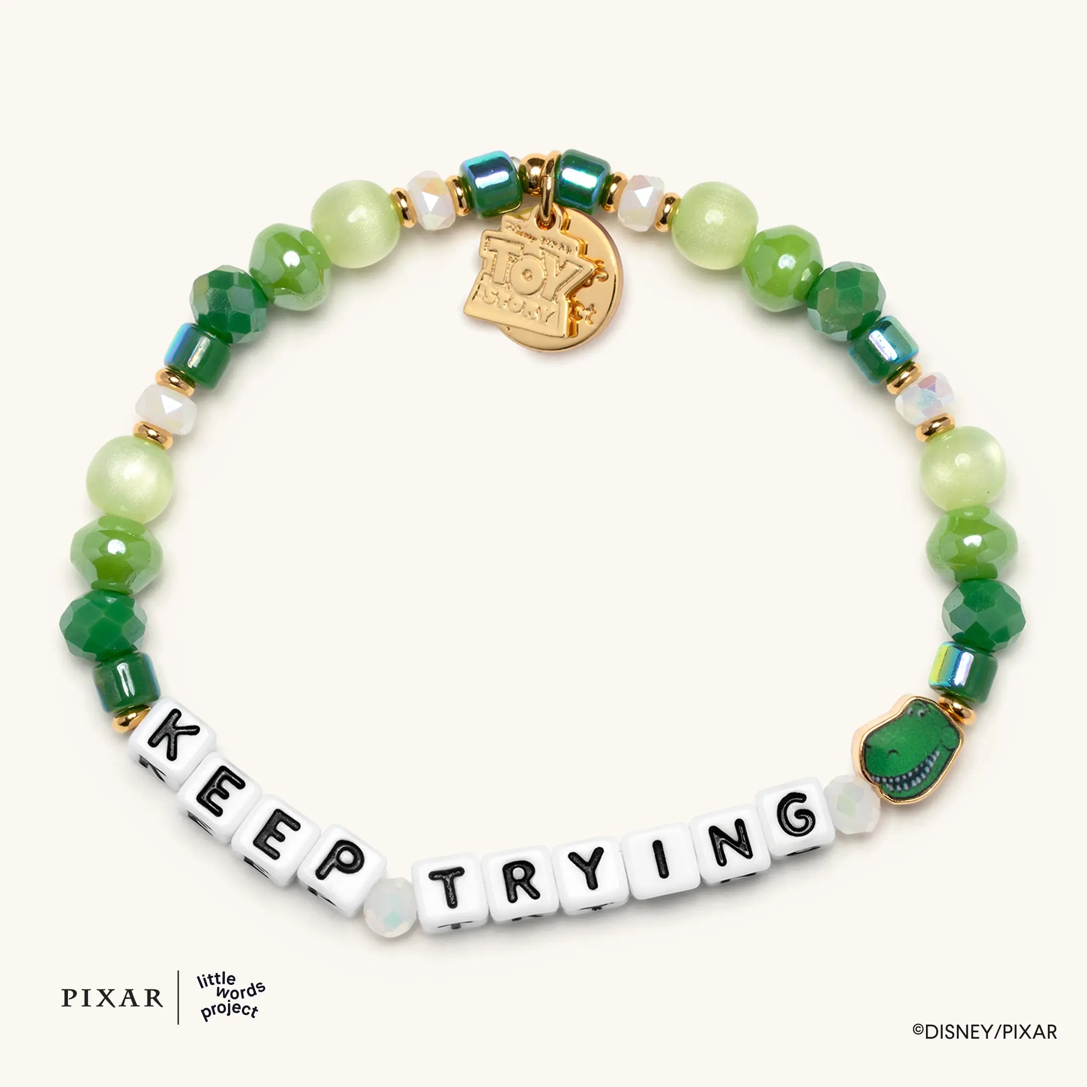 Keep Trying Toy Story bracelet, green beads spelling KEEP TRYING with a gold charm and green Rex charm, flat lay