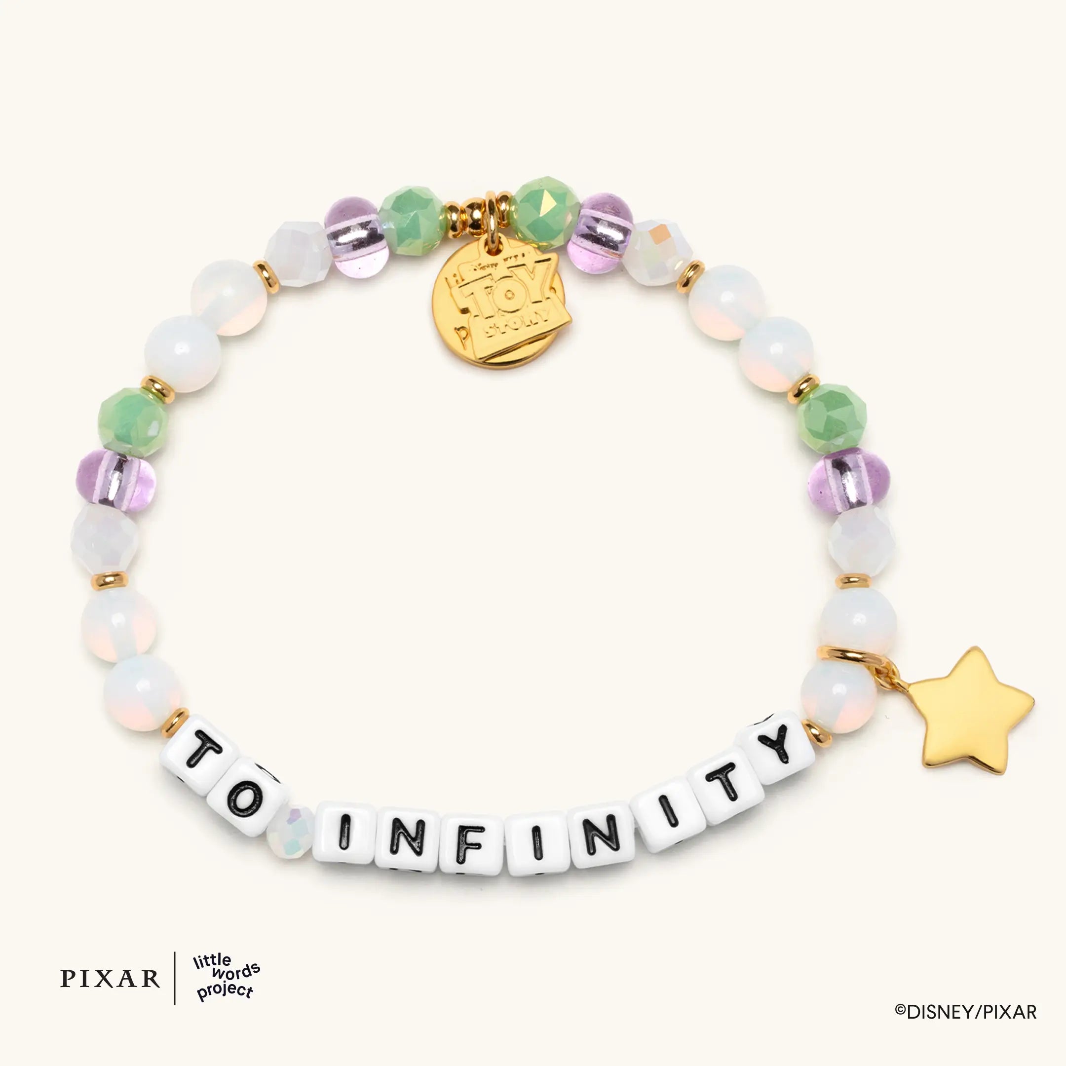 To Infinity Toy Story bracelet, white, green and purple beads spelling TO INFINITY with a gold charm and gold star charm, flat lay