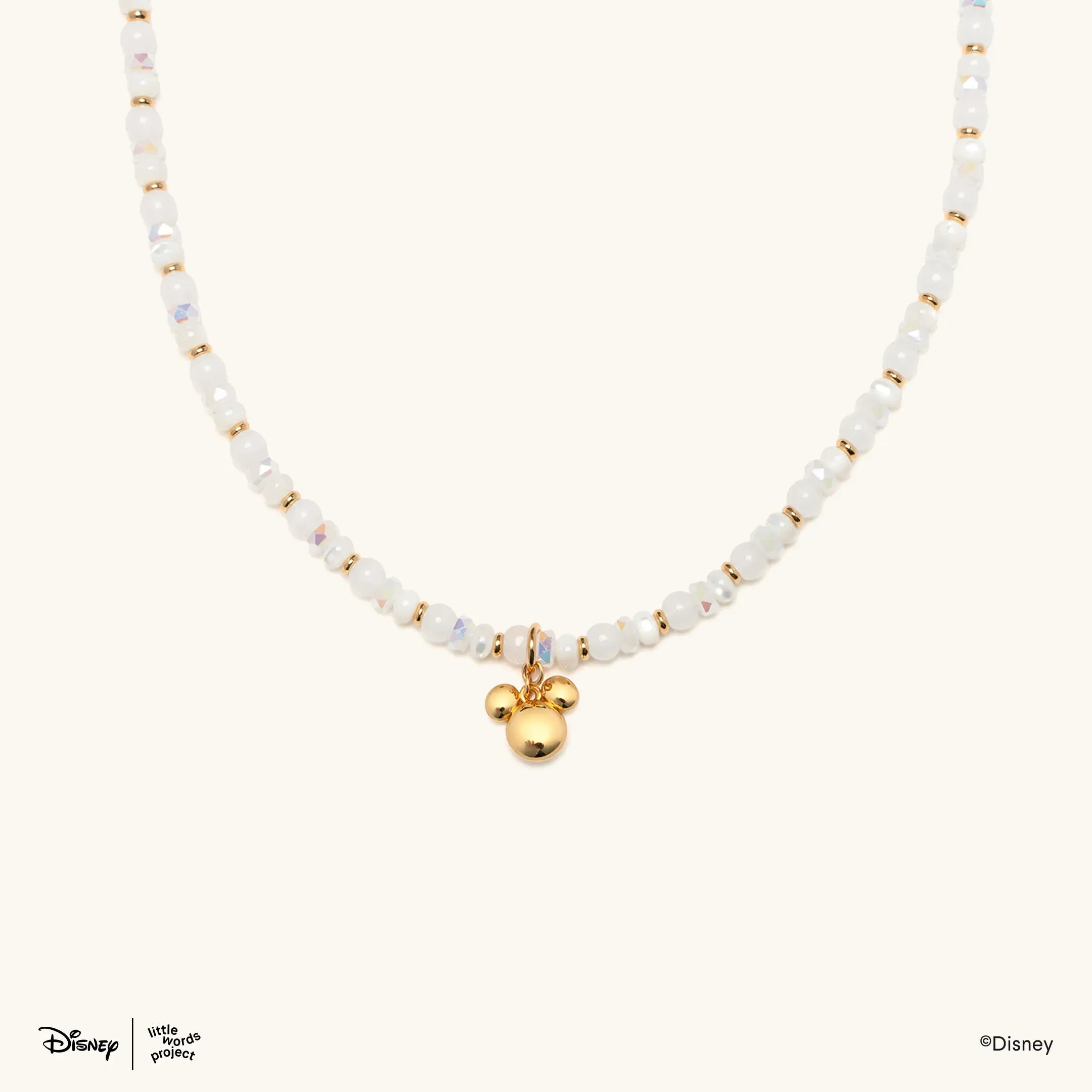 Mickey Mouse Charm Necklace from Disney Mickey and Friends, flat lay on cream with white and iridescent beads and a gold plated Mickey Mouse head pendant