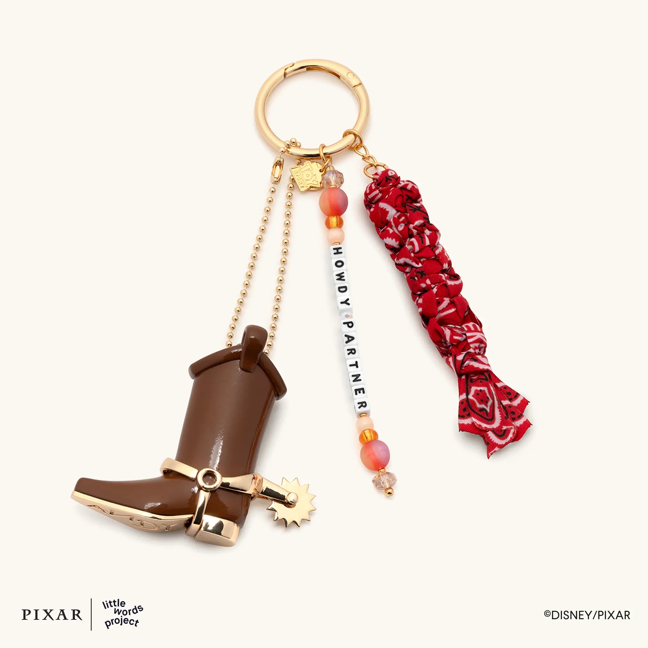 Howdy Partner Toy Story bag charm, brown cowboy boot, red bandana and HOWDY PARTNER beaded strand on a gold ring, flat lay