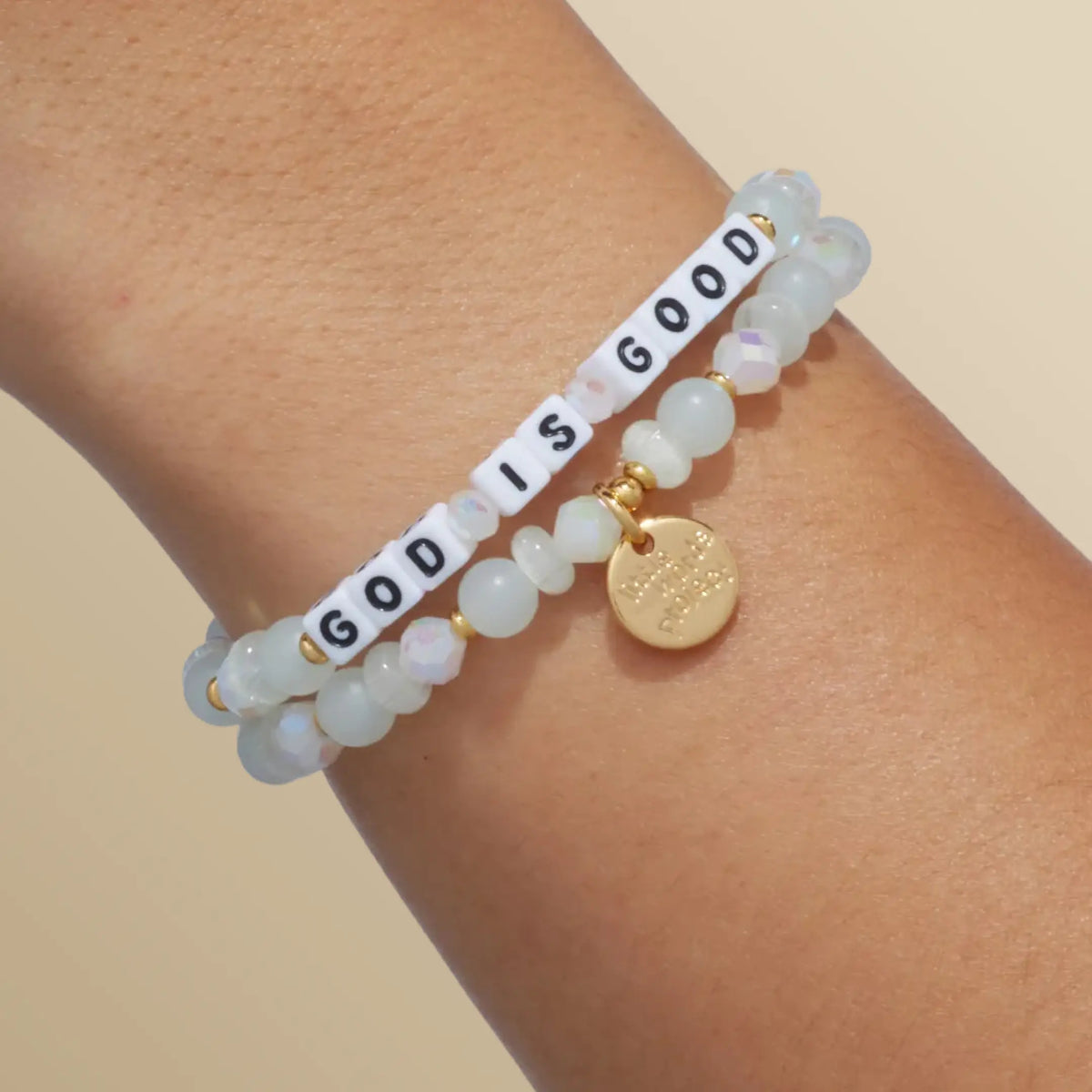God is Good bracelet in the Luxe Knit bead pattern with white letter beads, stacked with a second bracelet, on-model wrist shot on warm neutral background