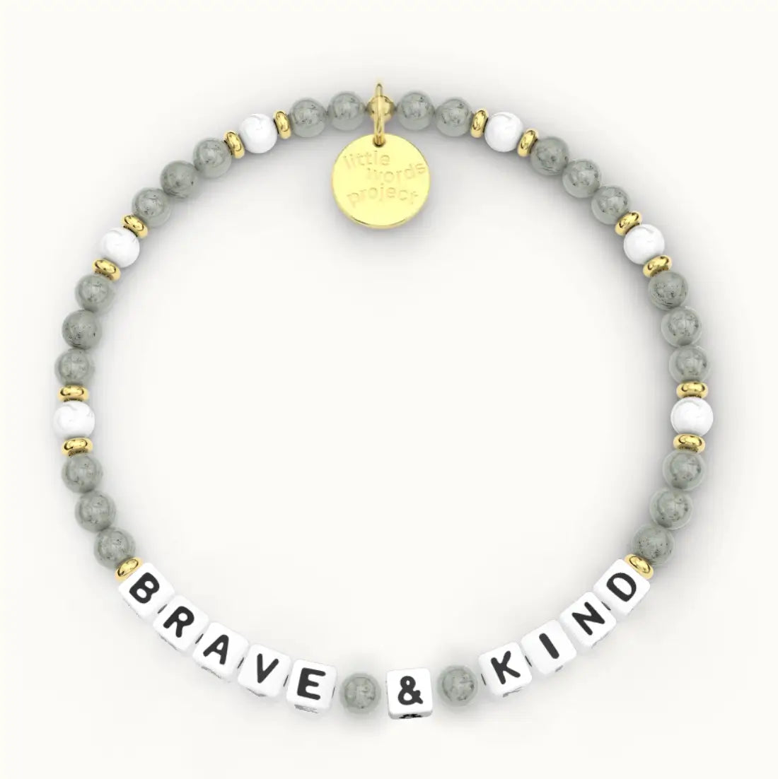 Brave & Kind giveback bracelet in the Sea Salt bead pattern, white letter beads with gray stone and white beads with gold accents, flat-lay on cream background