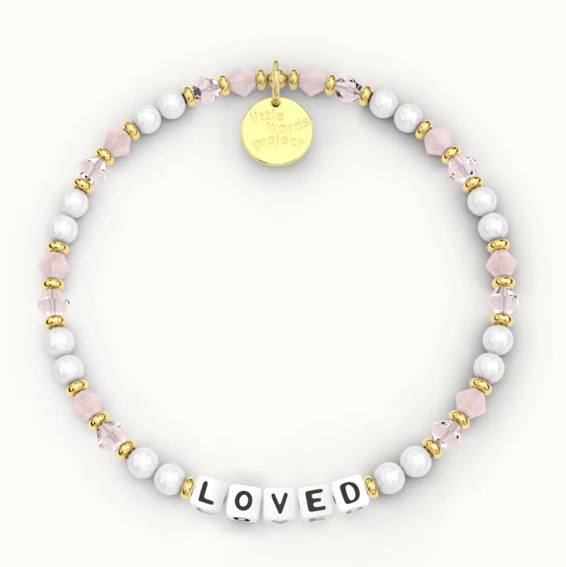 Loved giveback bracelet in the Pink Chalk bead pattern, white letter beads with white pearls and blush pink crystal beads with gold accents, flat-lay on cream background
