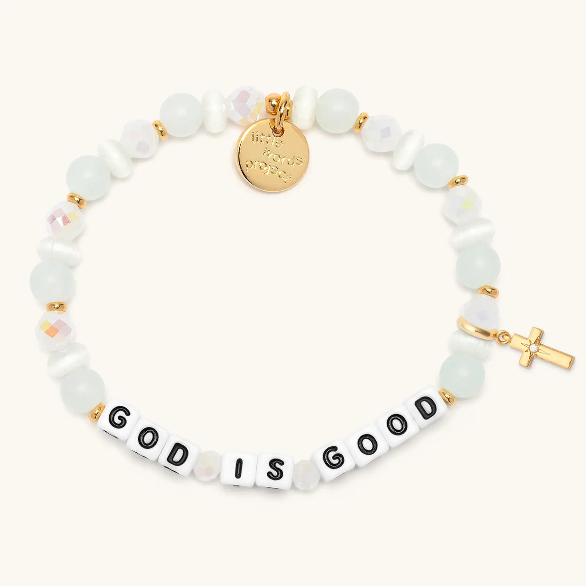 God is Good bracelet in the Luxe Knit bead pattern with white letter beads, gold puffy cross charm with a clear CZ stone, flat-lay on cream background