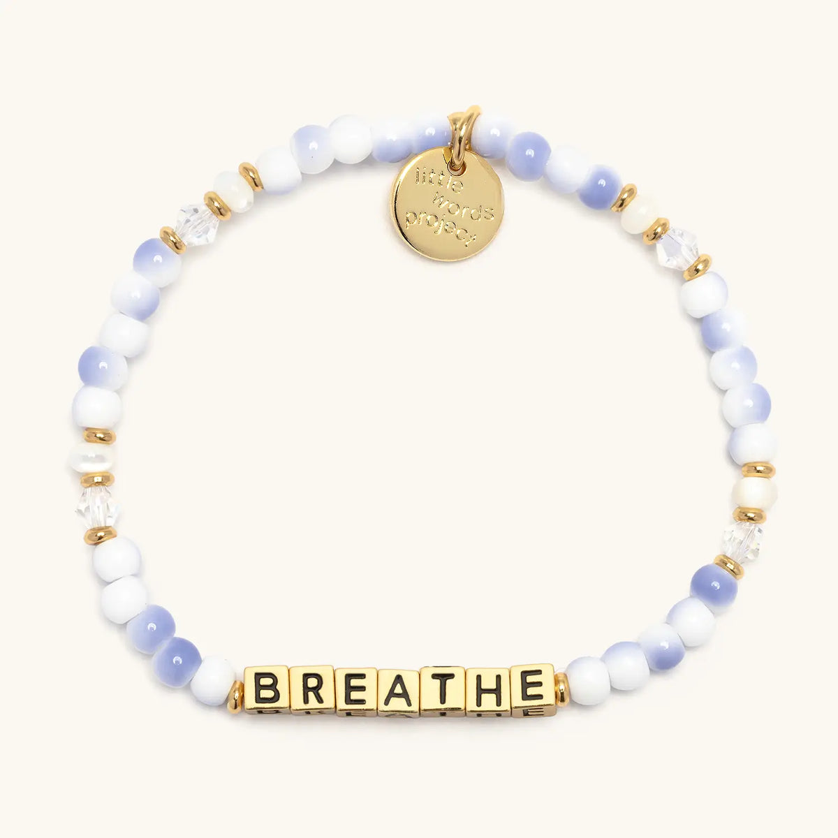 Gold Breathe bracelet in the Cotton Clouds bead pattern, gold letter beads with periwinkle and white swirl beads, white pearls, and clear crystals with gold accents, flat-lay on cream background