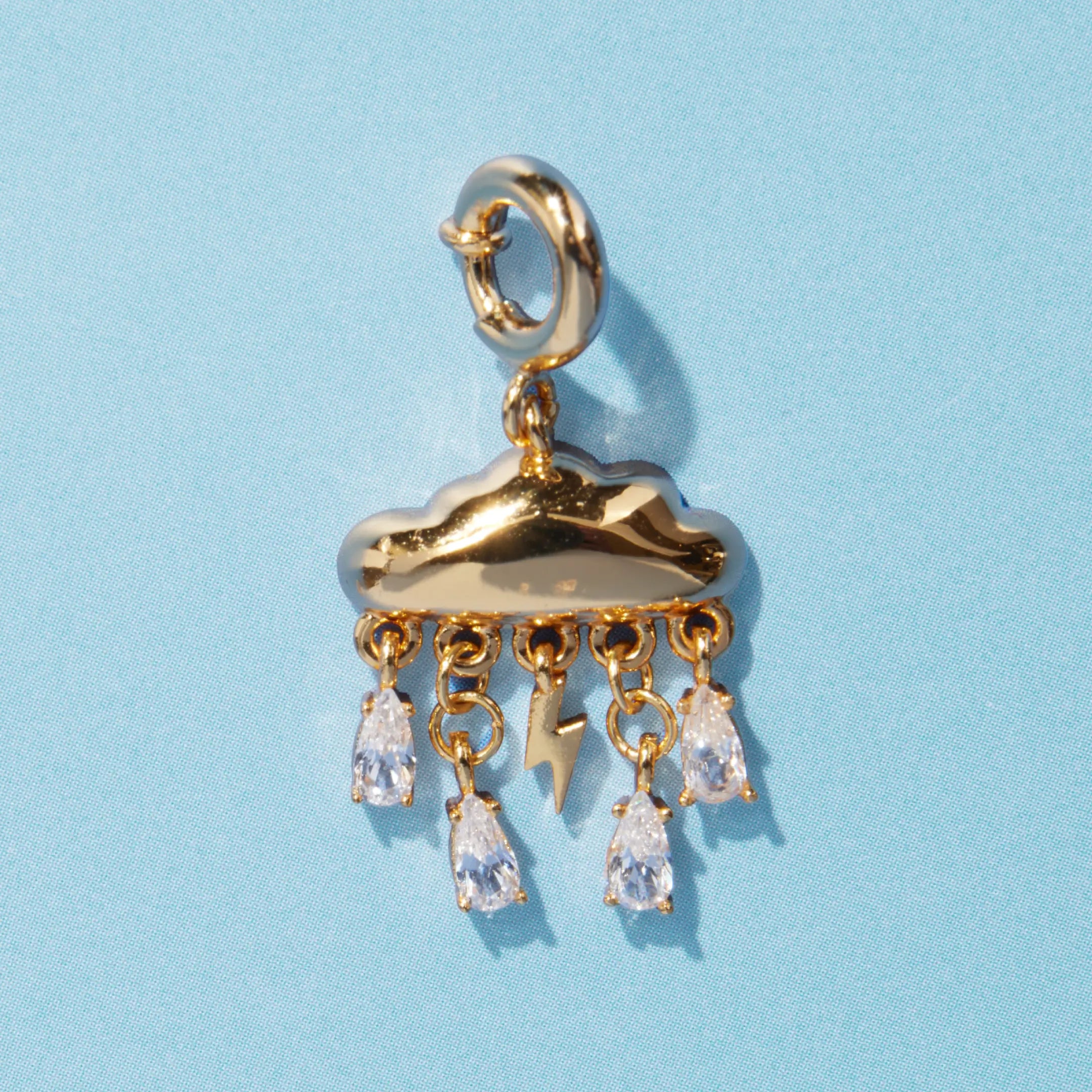 A gold cloud charm with a lightning bolt and five dangling crystal teardrop rhinestones, attached to a spring ring clasp, on a blue background.